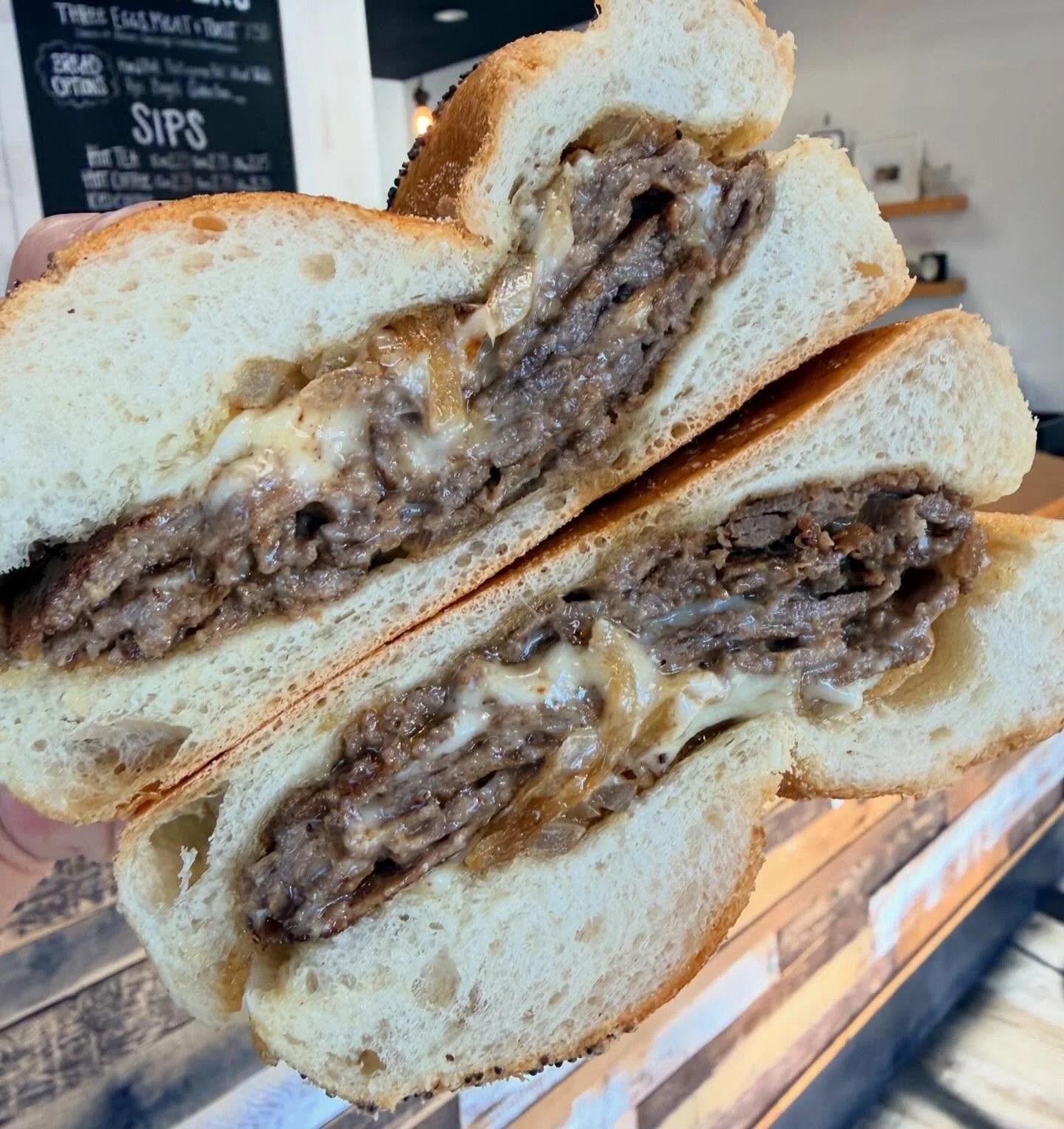 Close-up of a sliced garlic bread with cheesy beef filling inside, displayed on a wooden surface in a restaurant setting.