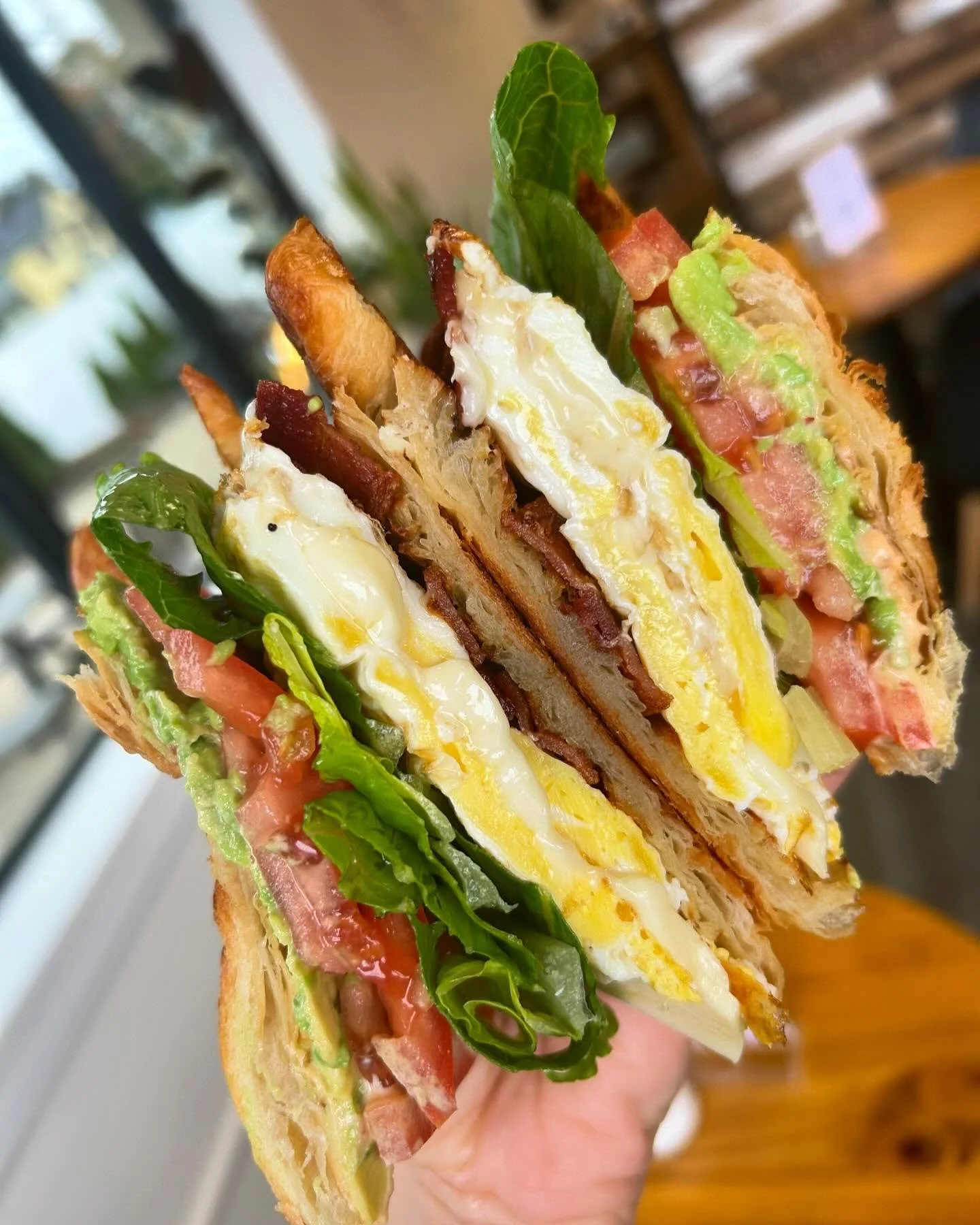 Close-up of a toasted sandwich with eggs, bacon, lettuce, tomato, and green leafy herbs.