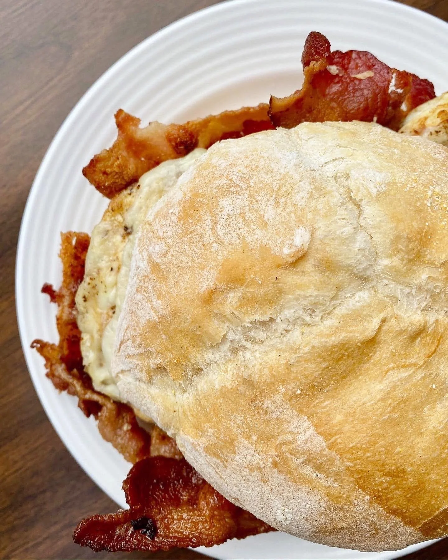 Close-up of a bacon, egg, and cheese breakfast sandwich on a bun served on a white plate.