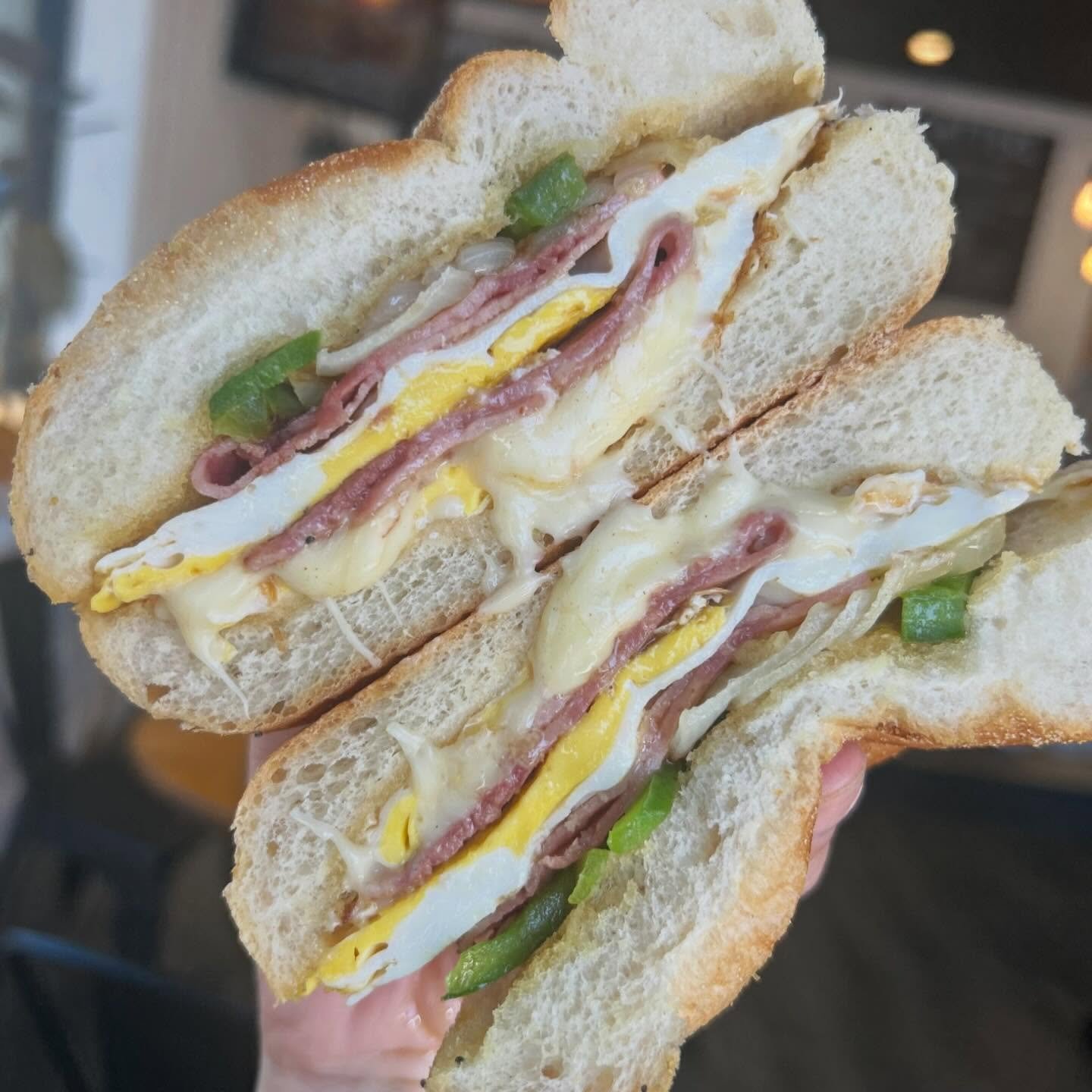 Close-up of a breakfast sandwich with eggs, bacon, green peppers, and shredded cheese on toasted bread.