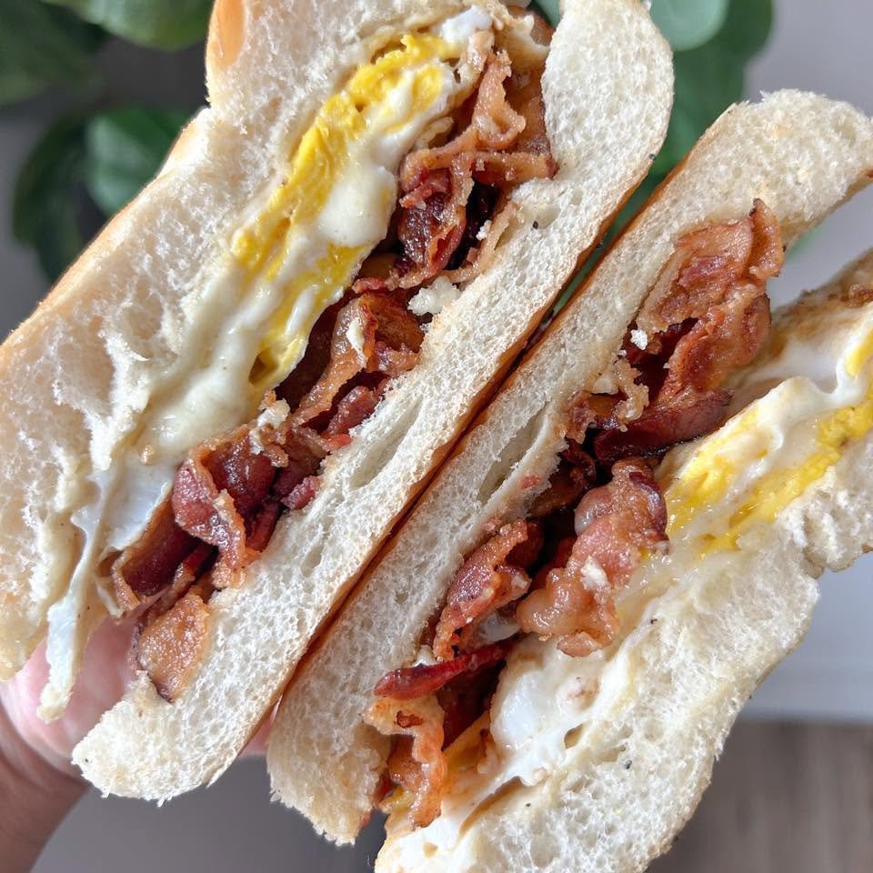 Close-up of a bacon, egg, and toast sandwich with crispy bacon and fried egg slices in between slices of white bread.