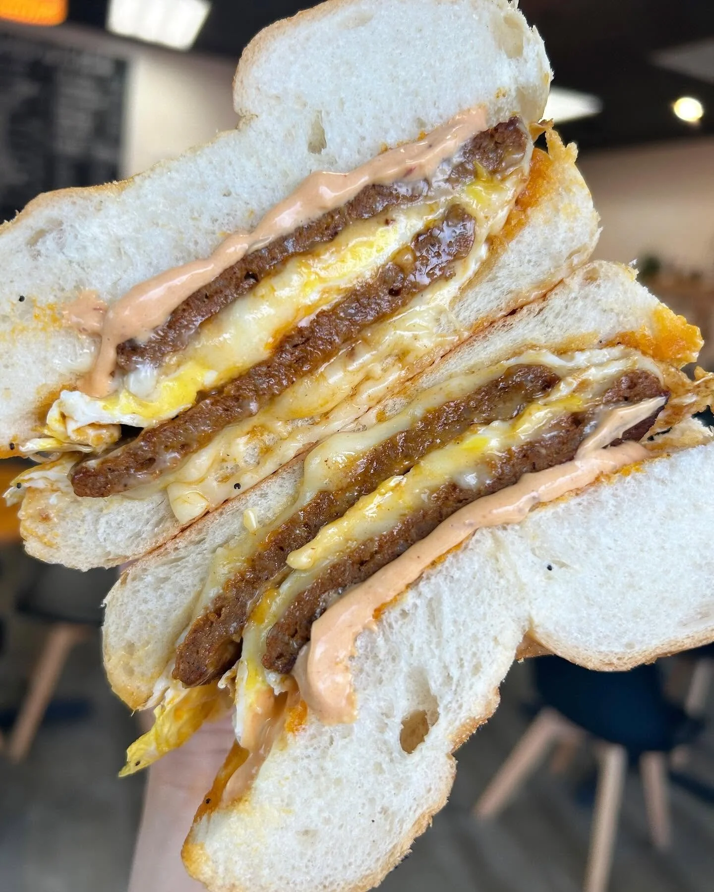 Close-up of a sandwich with fried egg, beef patty, cheese, and sauce on white bread.