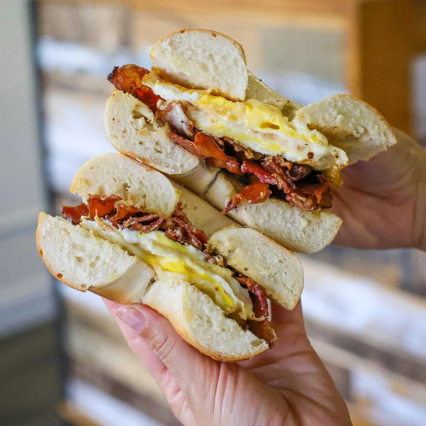 Close-up of a breakfast sandwich with bacon, eggs, and bread held in hand.