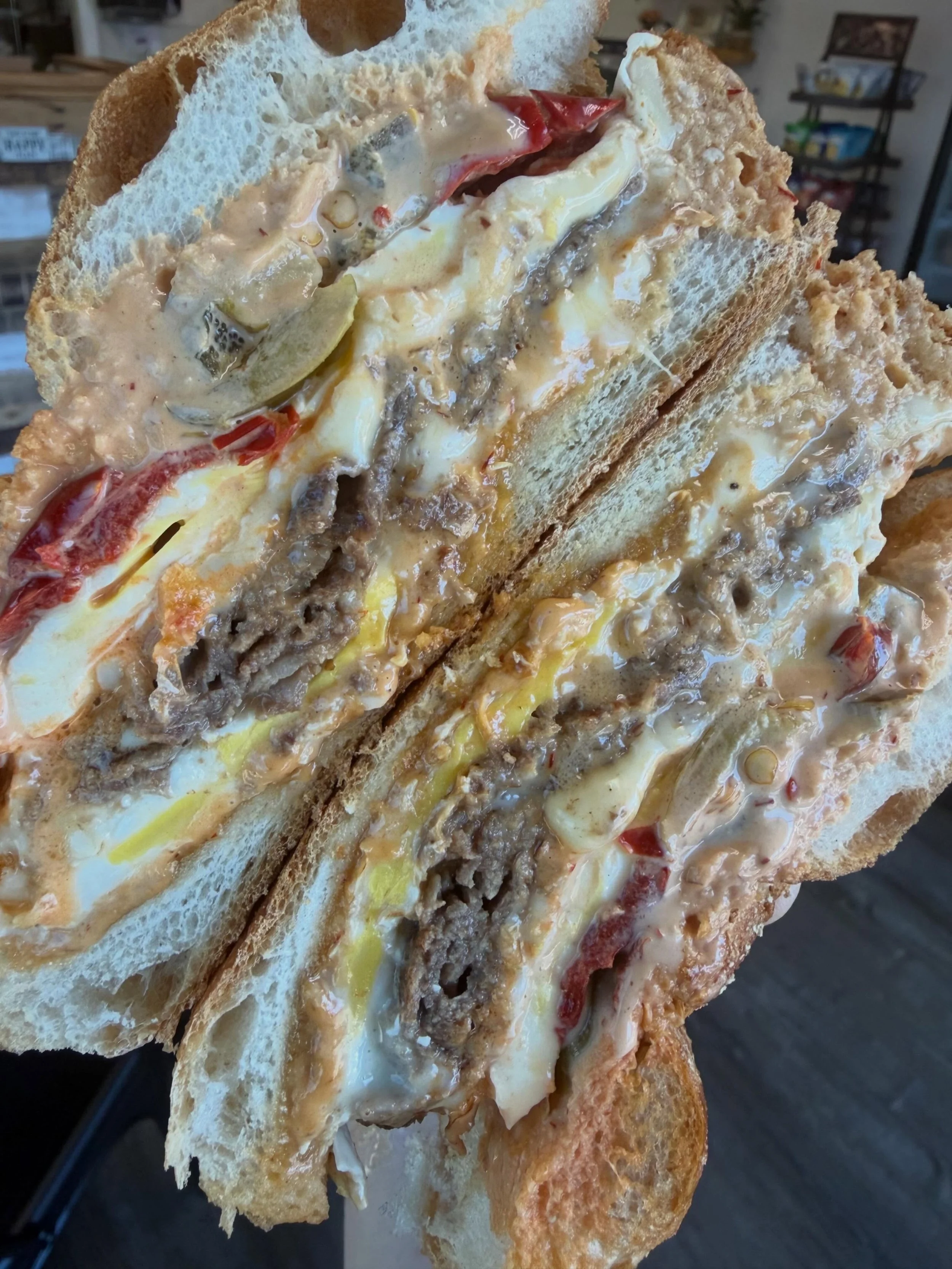 Close-up of a toasted sandwich filled with melted cheese, sliced pickles, red bell peppers, and ground meat.