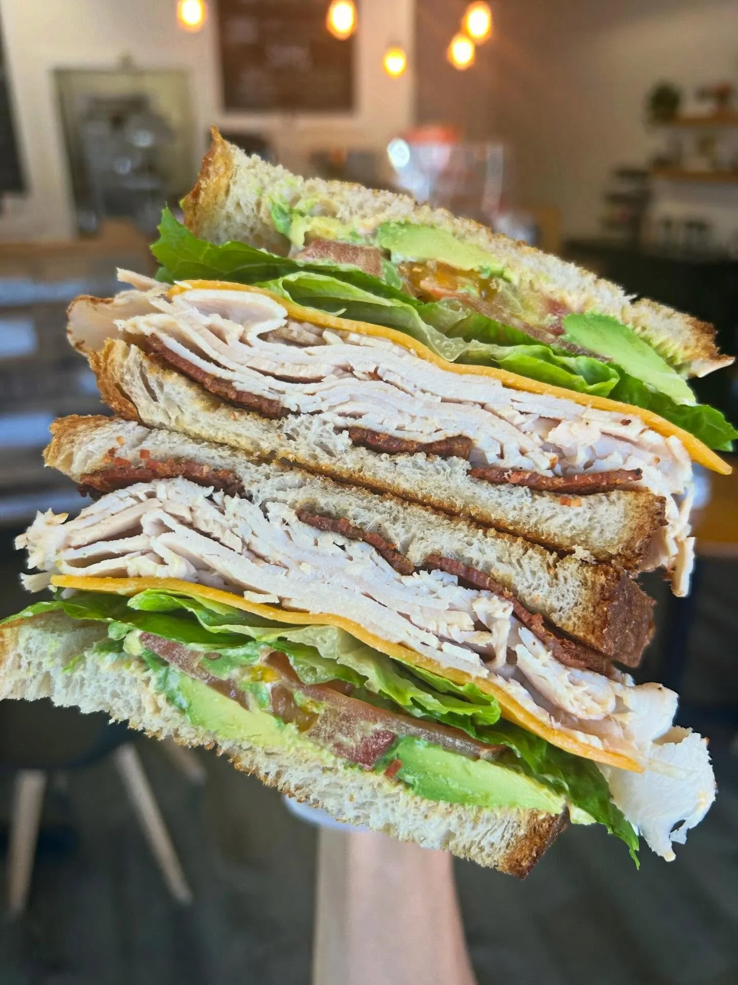 Close-up of a stacked club sandwich with layers of turkey, lettuce, tomato, cheese, and bacon between toasted bread slices.