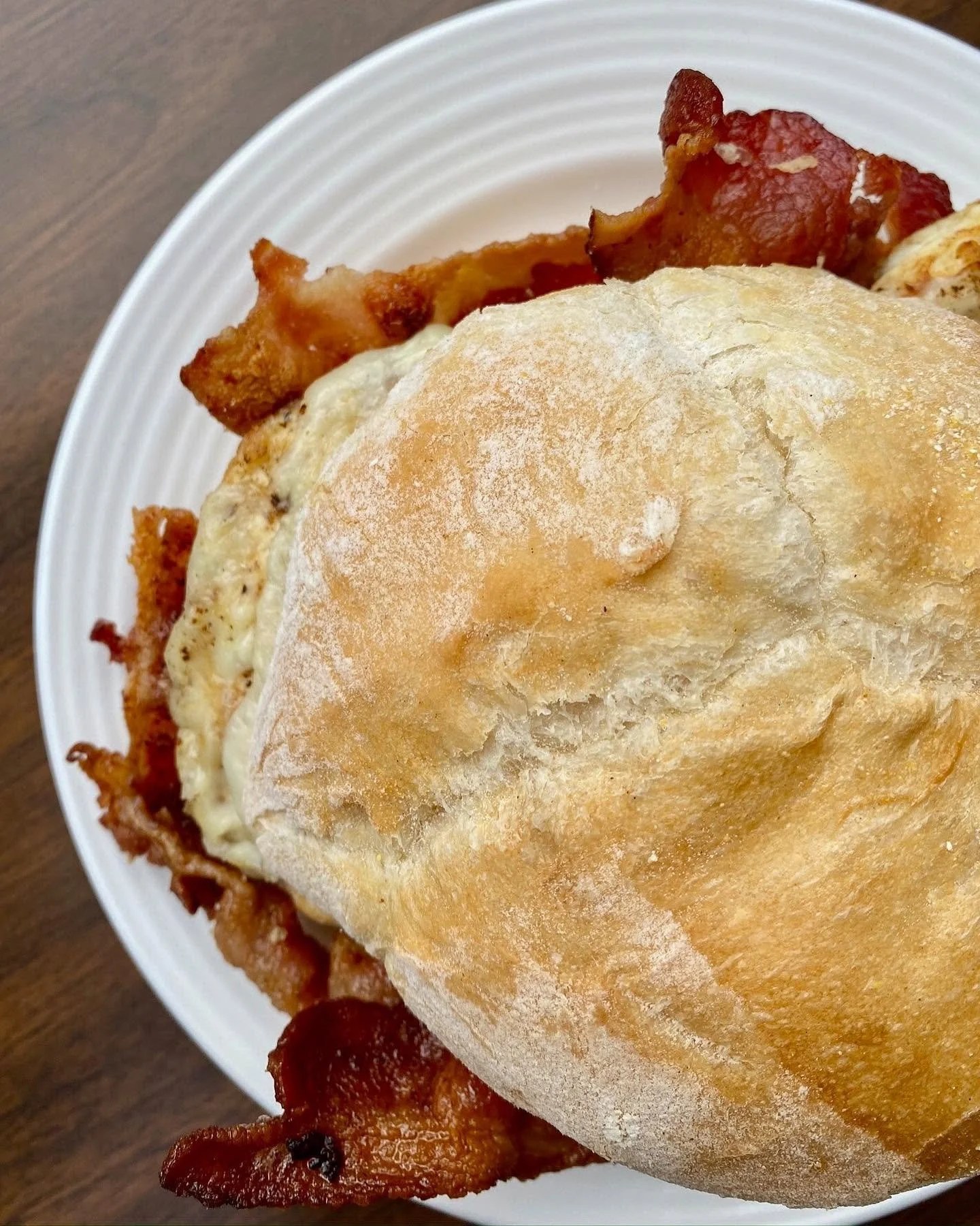 Bacon, scrambled eggs, and bread roll on a white plate.