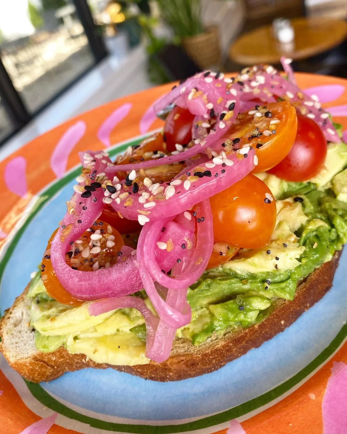 Open-faced sandwich with lettuce, cherry tomatoes, pickled onions, and sesame seeds on toasted bread.