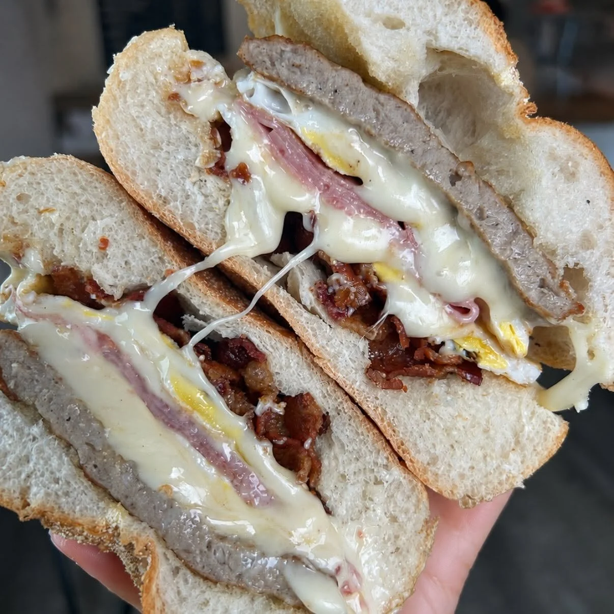 A quesadilla sandwich with melted cheese, bacon, sausage, ham, and egg in a toasted hoagie bun.