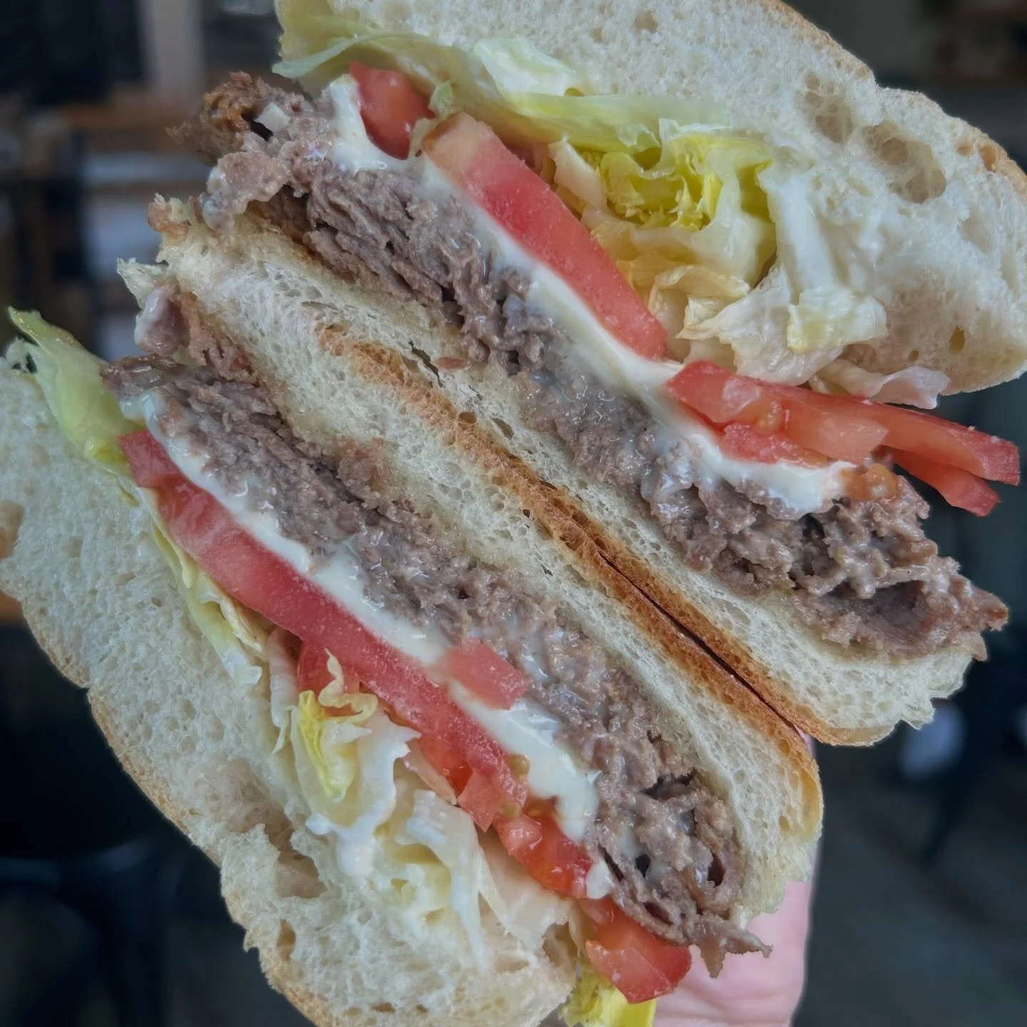 Close-up of a sliced sandwich with lettuce, tomato, ground beef, and mayonnaise on white bread.