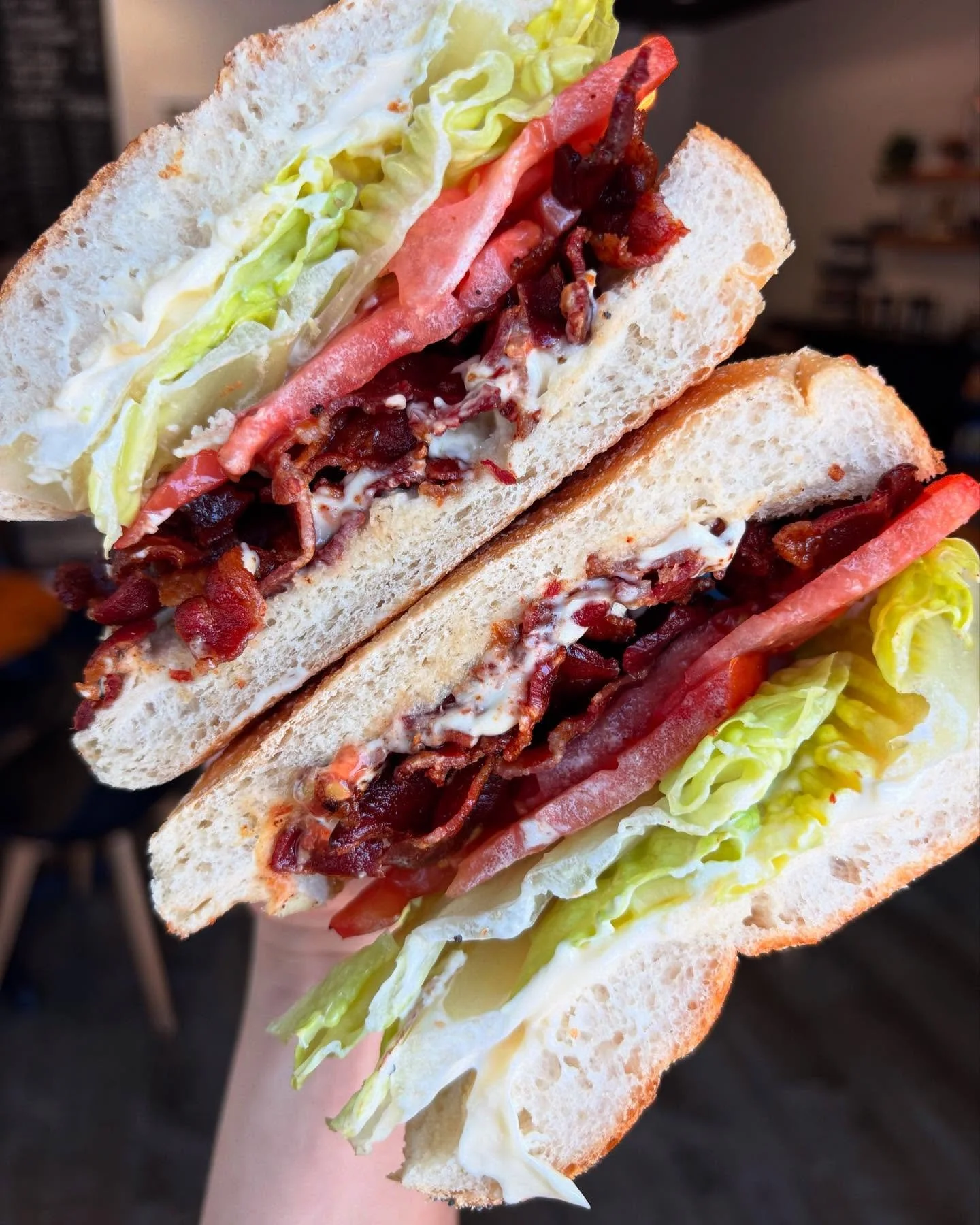 Close-up of a sandwich with lettuce, tomato, bacon, and mayonnaise on white bread.