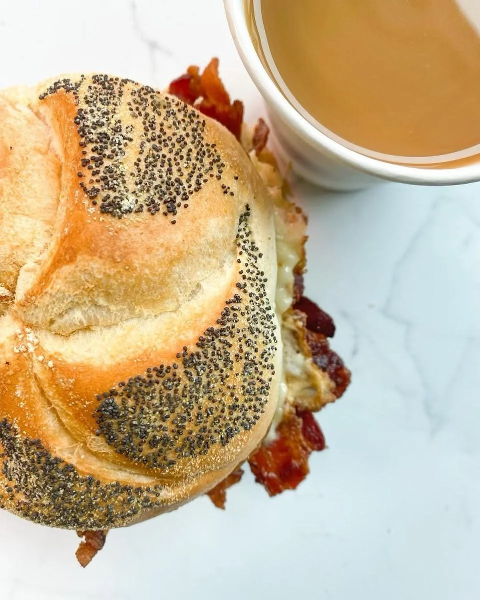 Poppy seed bagel sandwich with bacon, egg, and cheese, served with a cup of coffee or tea.