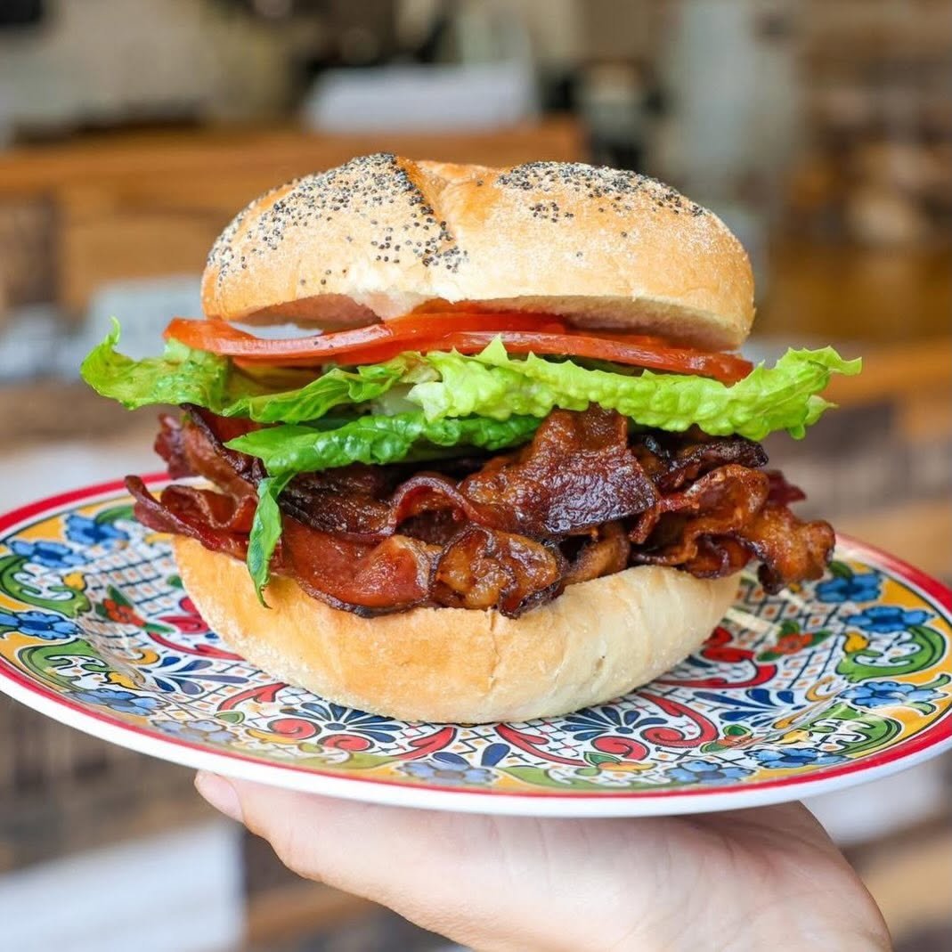 Close-up of a bacon, lettuce, tomato, and bacon sandwich on a colorful plate, held by a hand.