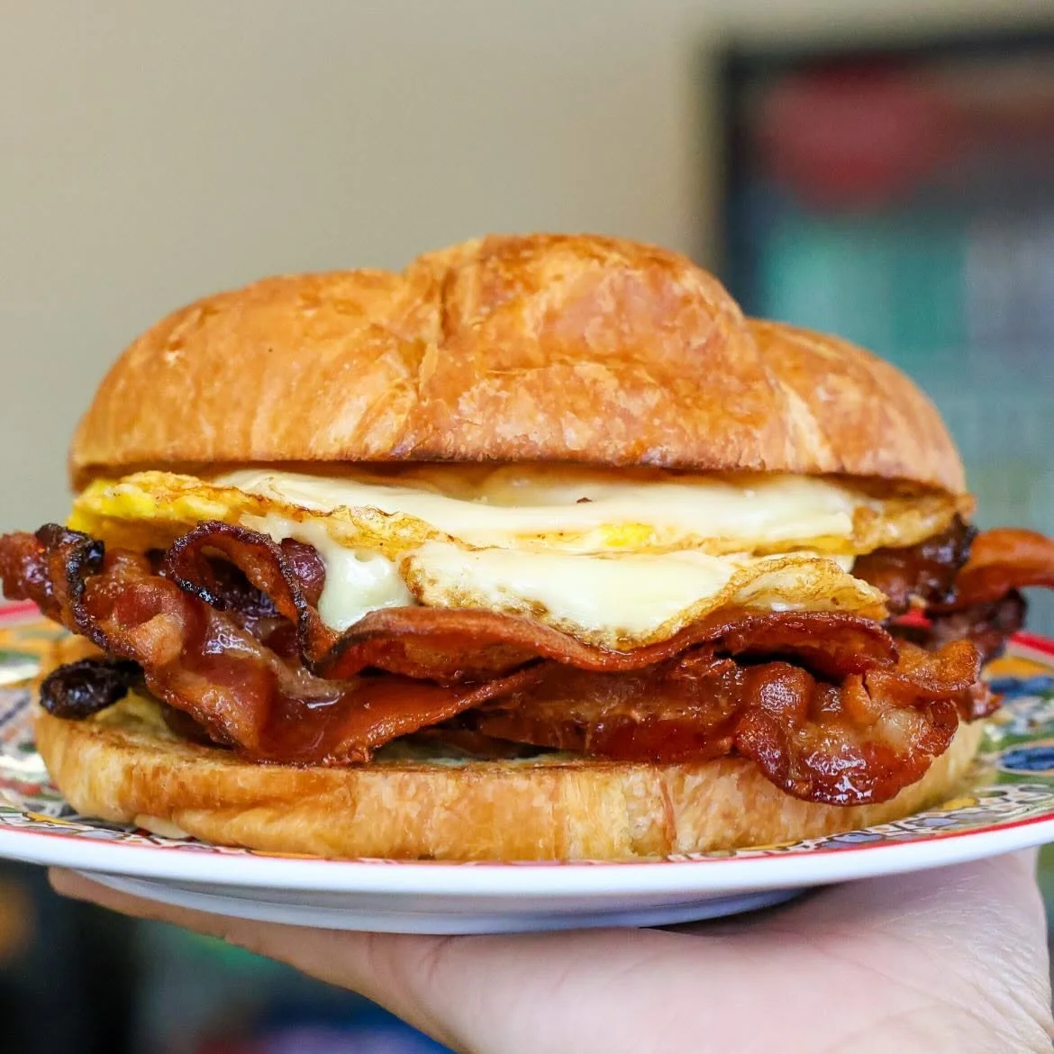 Bacon, fried eggs, and croissant sandwich on a plate.