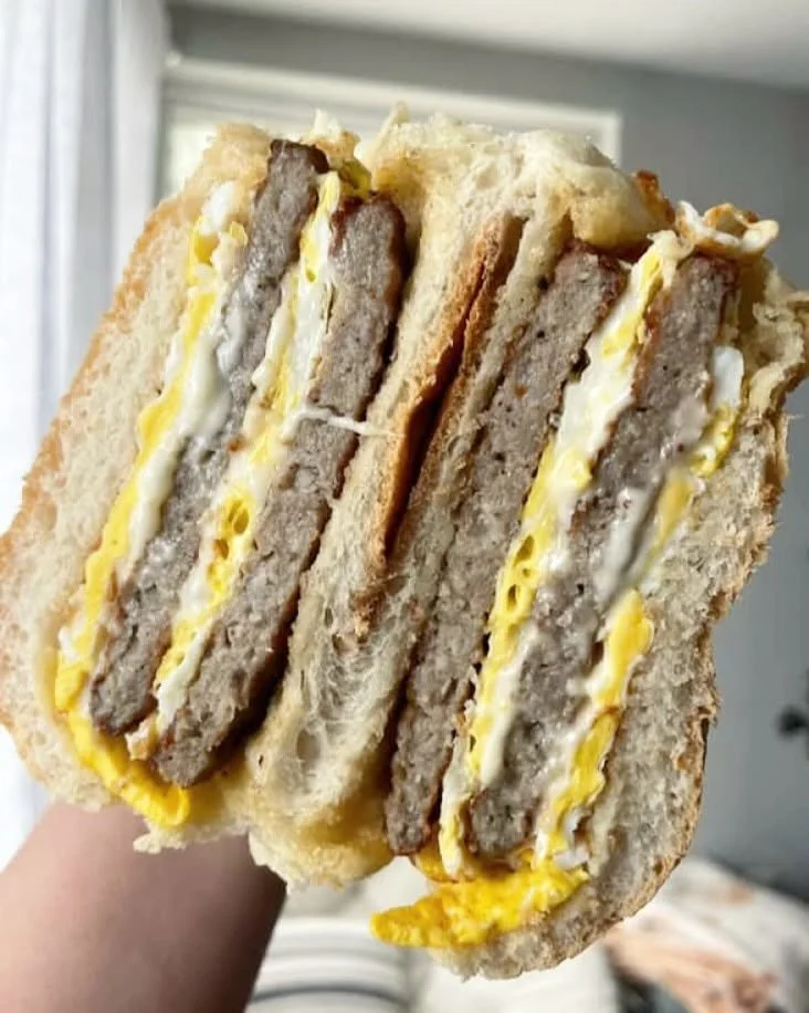 Close-up of a breakfast sandwich with sausage patties, scrambled eggs, and cheese on toasted bread.
