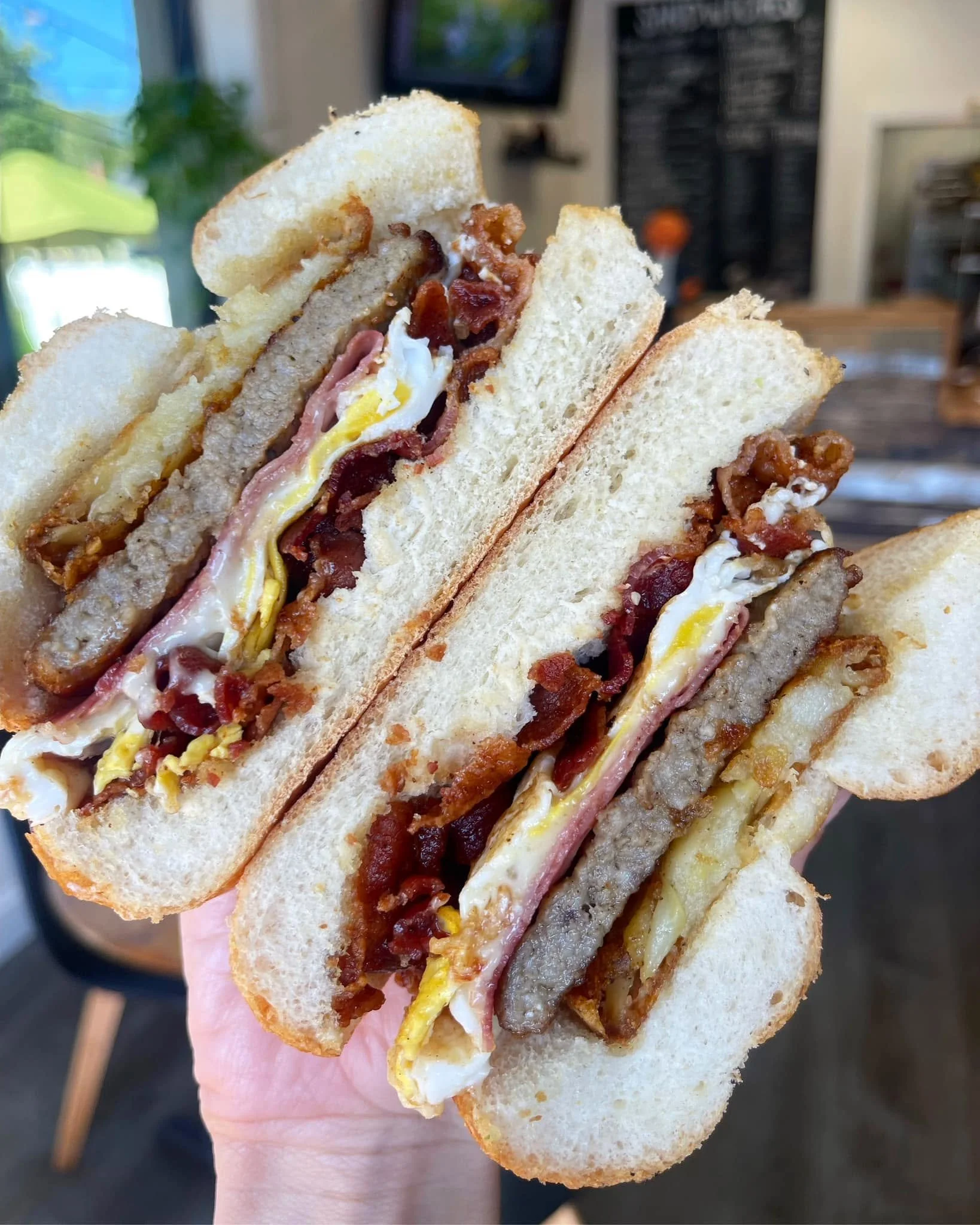Close-up of a sandwich with ham, bacon, egg, cheese, and bacon on white bread.