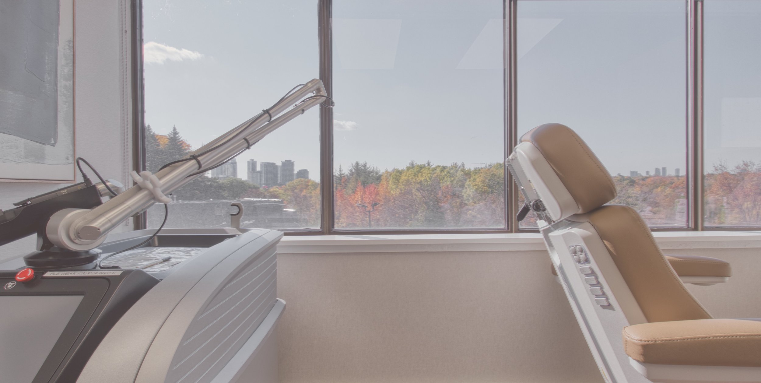 Modern dental office with a dental treatment chair and overhead examination light beside large windows overlooking autumn trees and city buildings