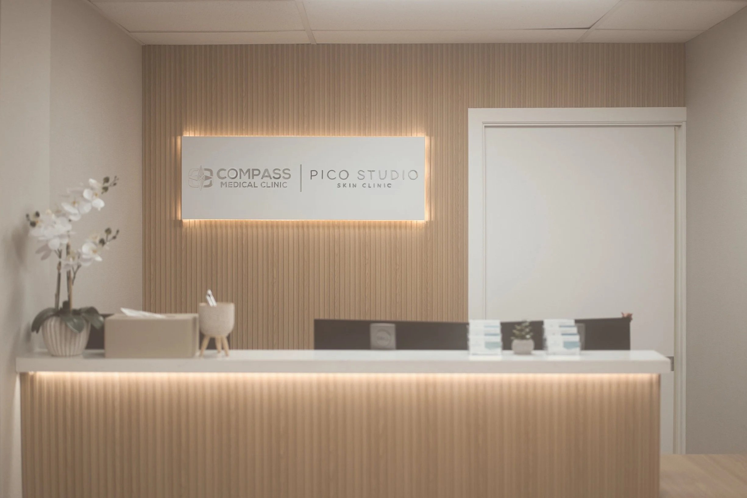 Reception desk at Compass Medical Clinic and Pico Studio Skin Clinic with illuminated signage and floral décor.