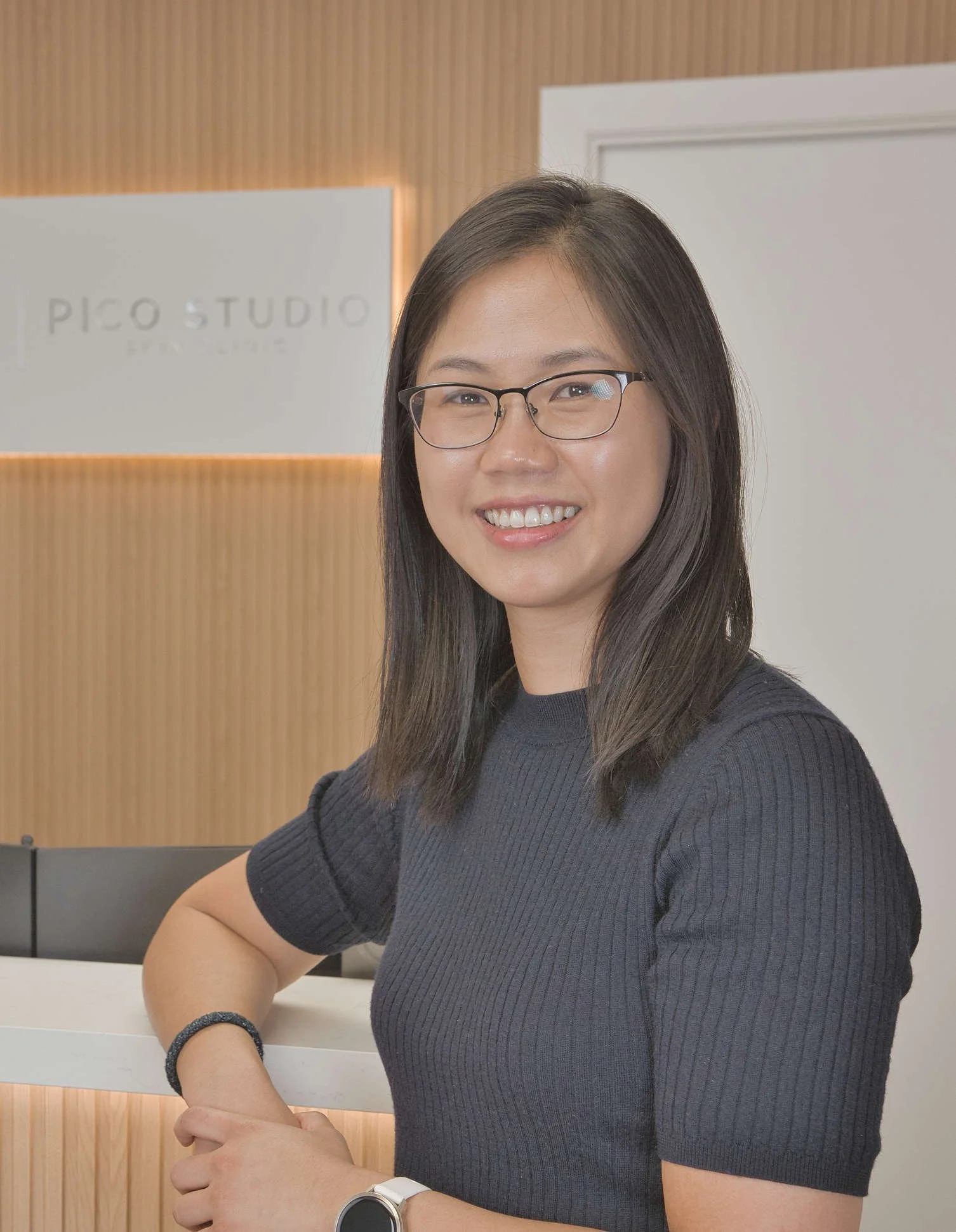 Smiling woman wearing glasses and a dark ribbed shirt in an office
