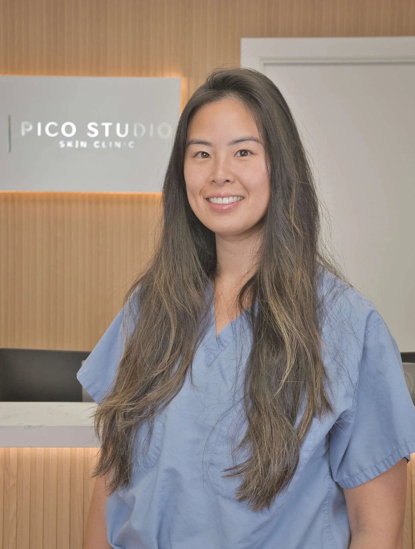 Smiling woman in blue medical scrubs standing in front of a Pico Studio Skin Clinic sign