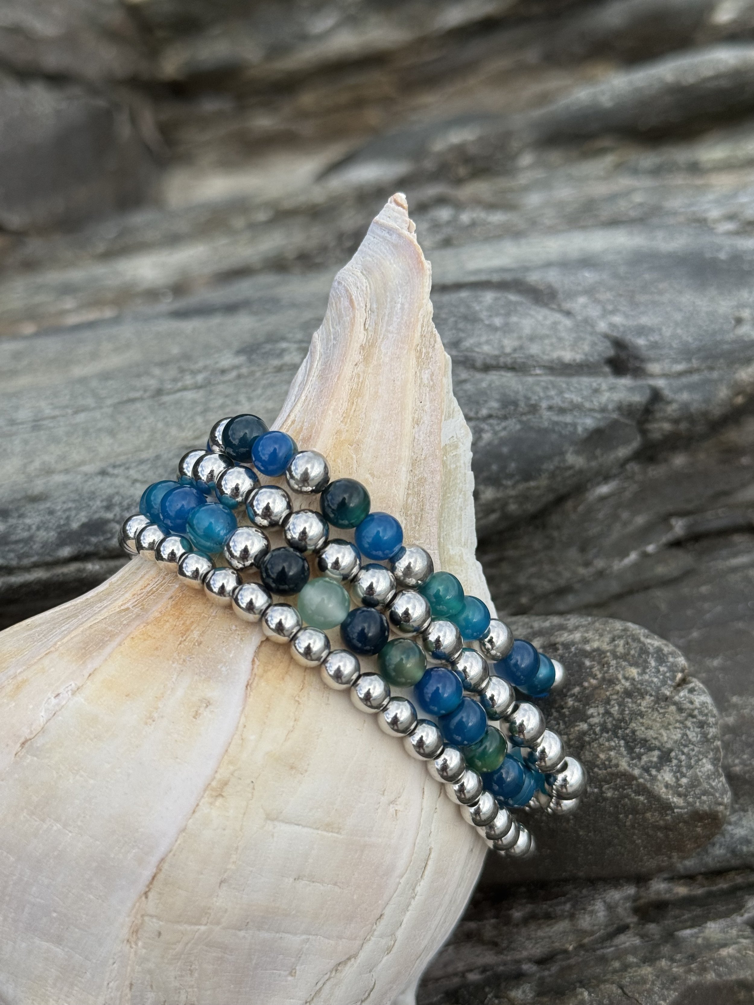 Colorful beaded bracelets draped over a white seashell on a rocky surface.