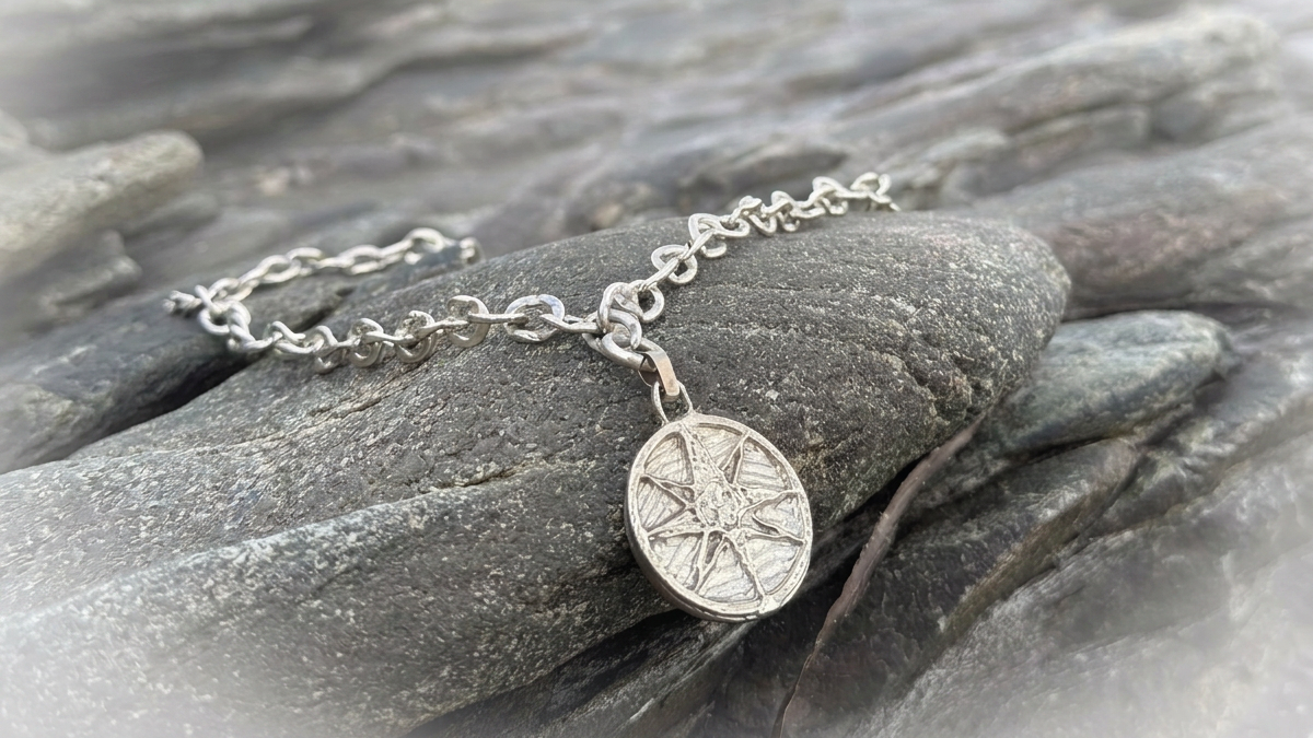 Silver compass rose pendant necklace featuring compass rose design, resting on a dark, textured rock surface.