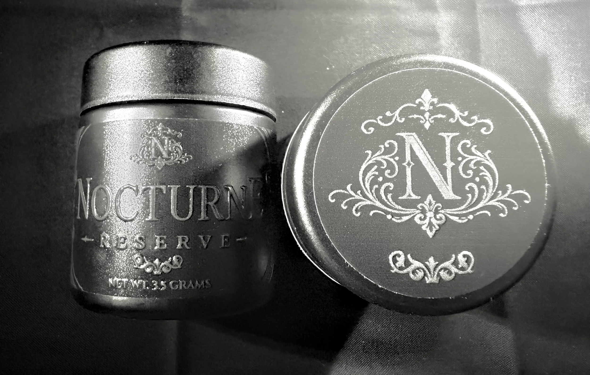 A metallic tin container with a lid, featuring decorative and elegant engravings including the initials 'N' and 'C'. The label on the container reads 'Nocoutner Reserve' and indicates it contains 113 grams.