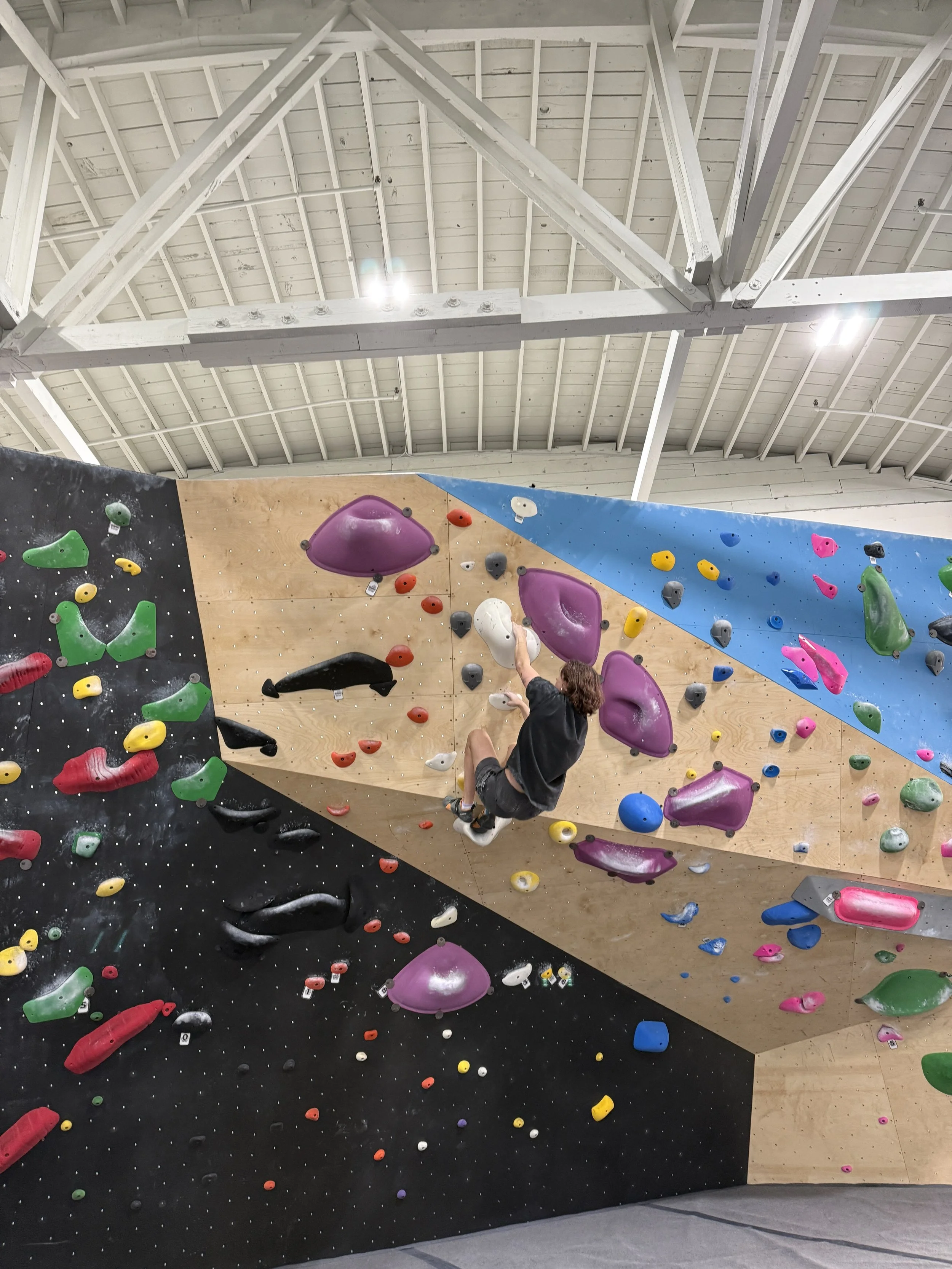 Indoor rock climbing gym with a person mid-climb on a colorful bouldering wall.