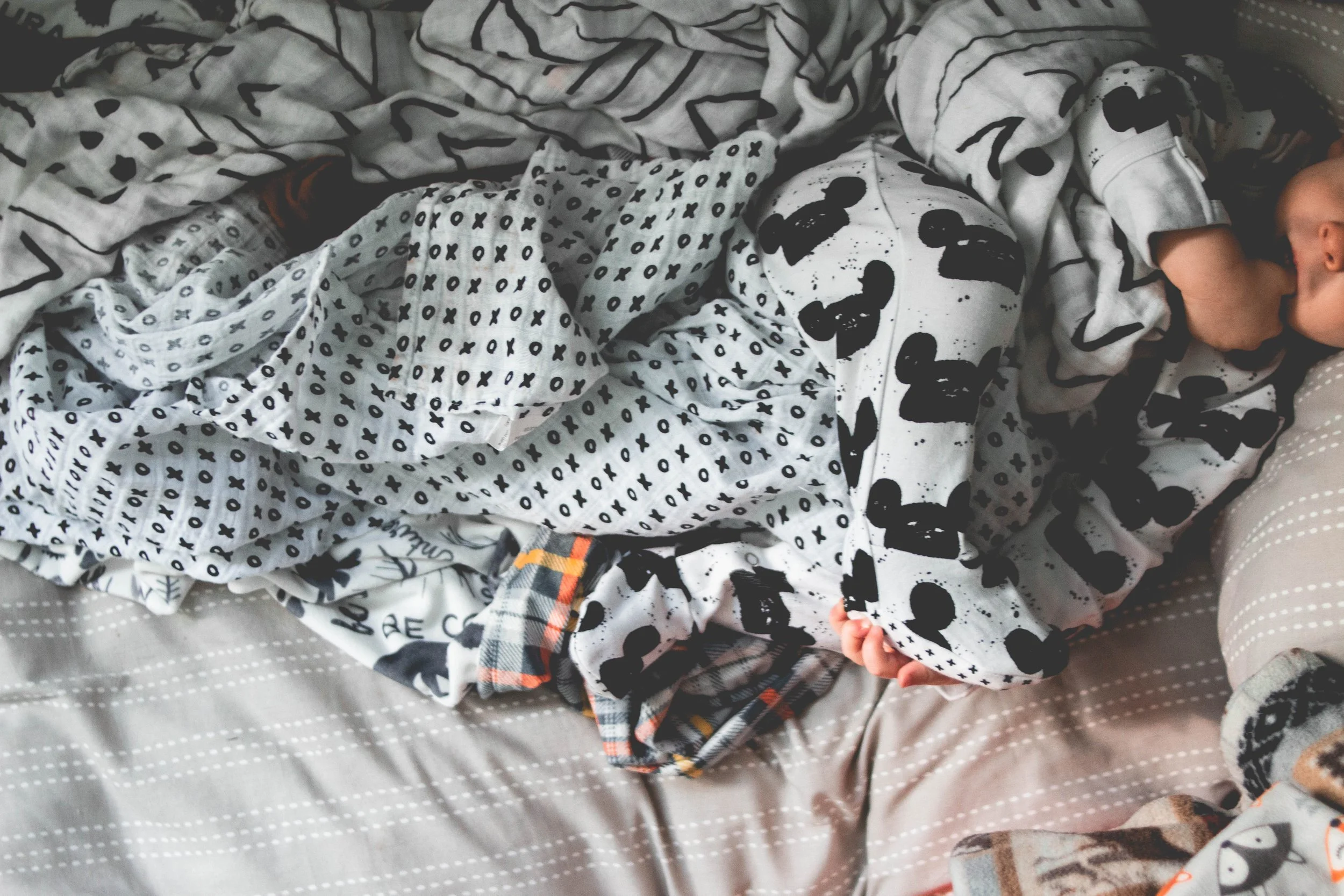 Close-up of a baby sleeping on a bed surrounded by patterned blankets and clothes.