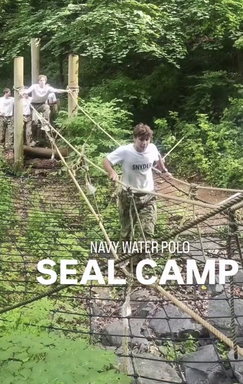 A group of boys crossing a suspension bridge over a creek surrounded by lush green trees at Navy Water Polo Seal Camp.