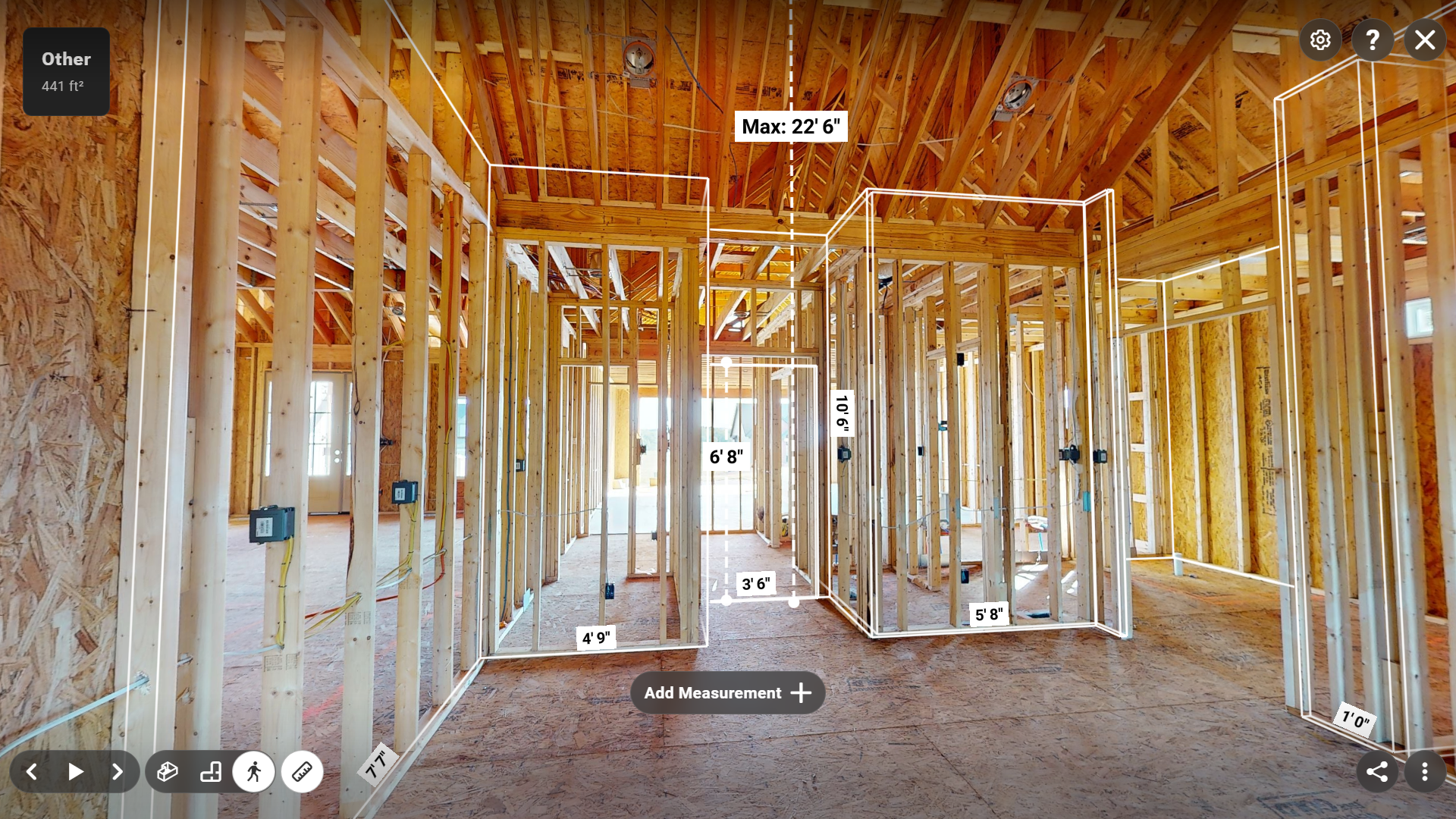 Interior view of a house under construction showing wooden framing with measurements, electrical wiring, and some lighting fixtures installed.