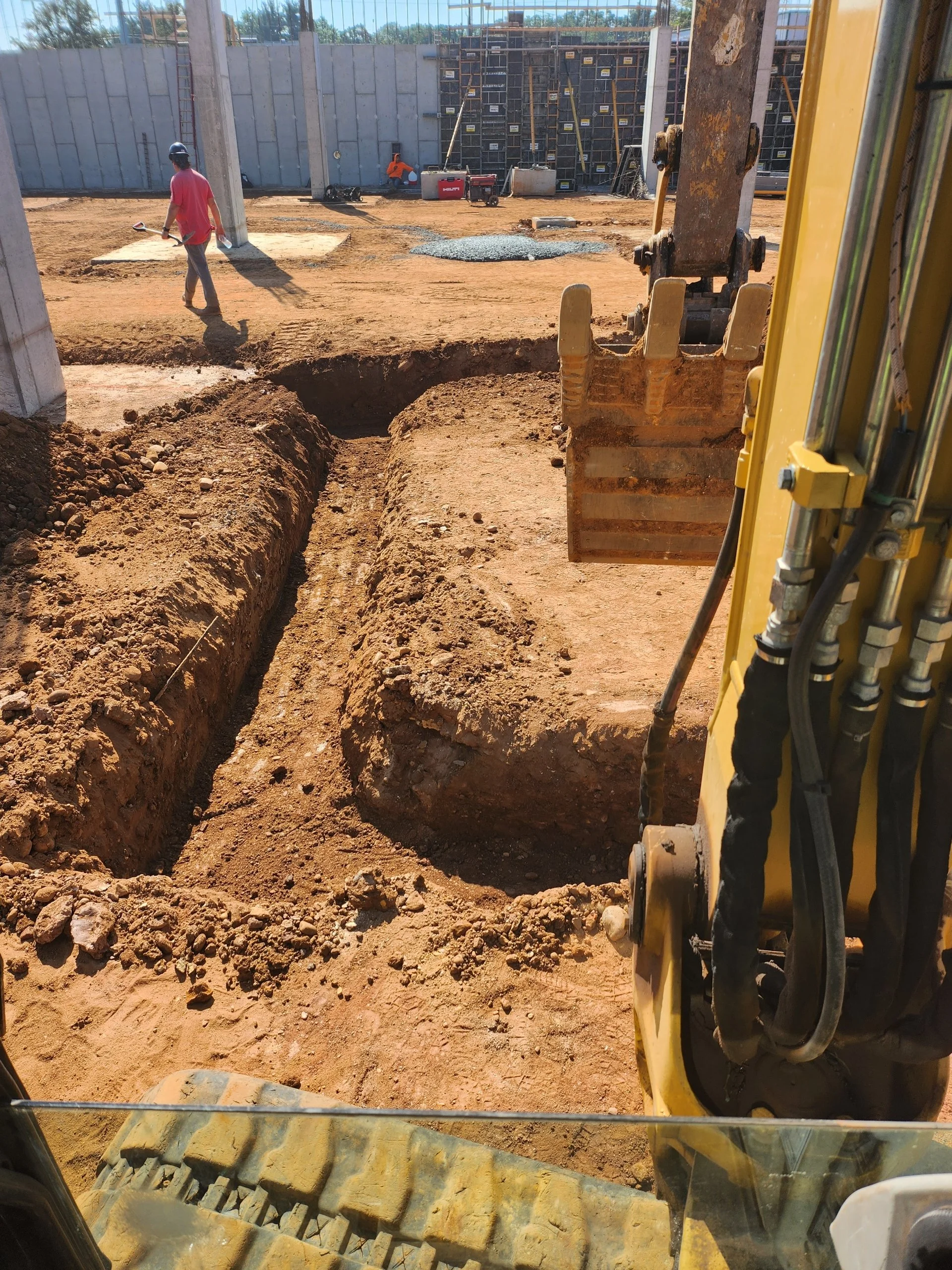 View from inside a construction vehicle looking out onto a construction site with workers, dirt excavation, and partially built wall or foundation.