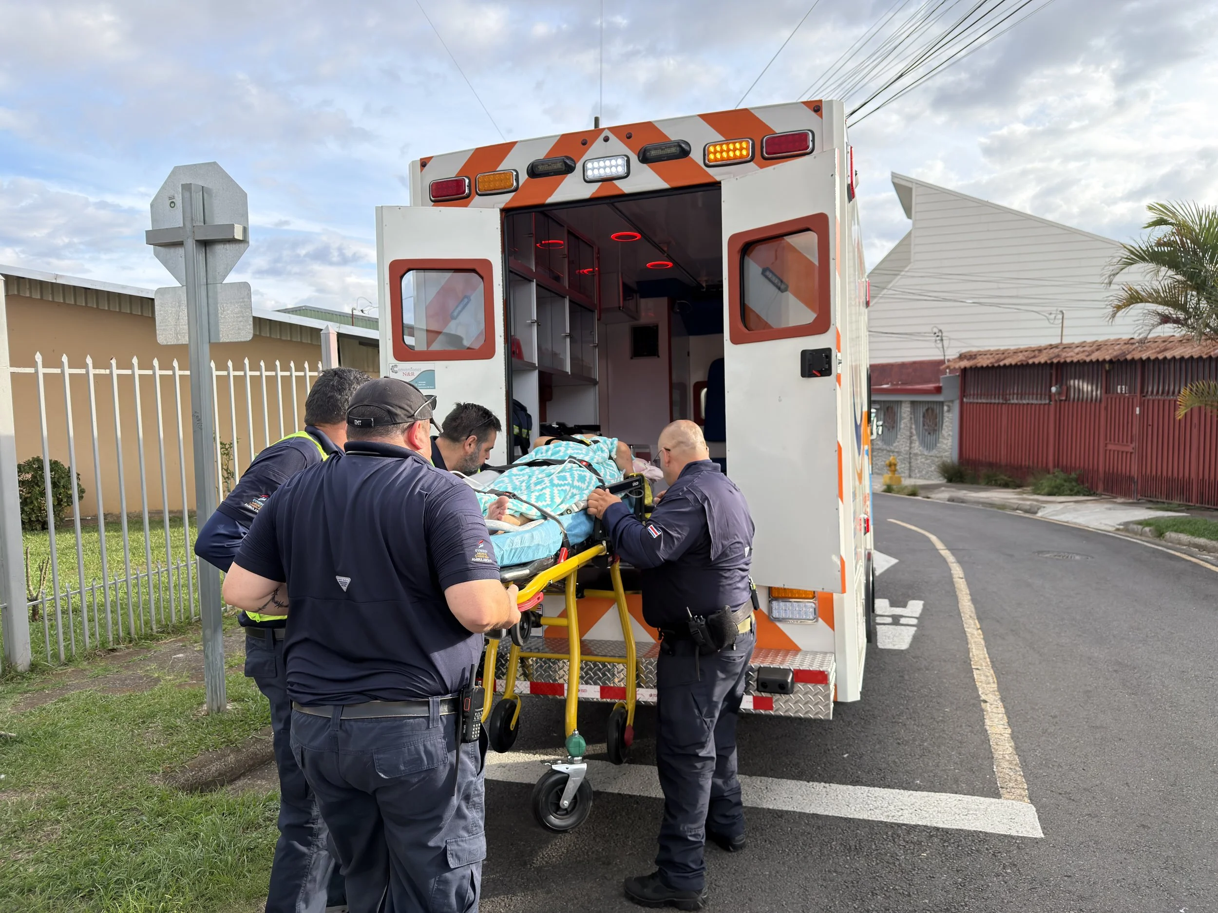 Paramedics loading a patient on a stretcher into an ambulance with emergency lights on, while several paramedics assist and prepare for transport.