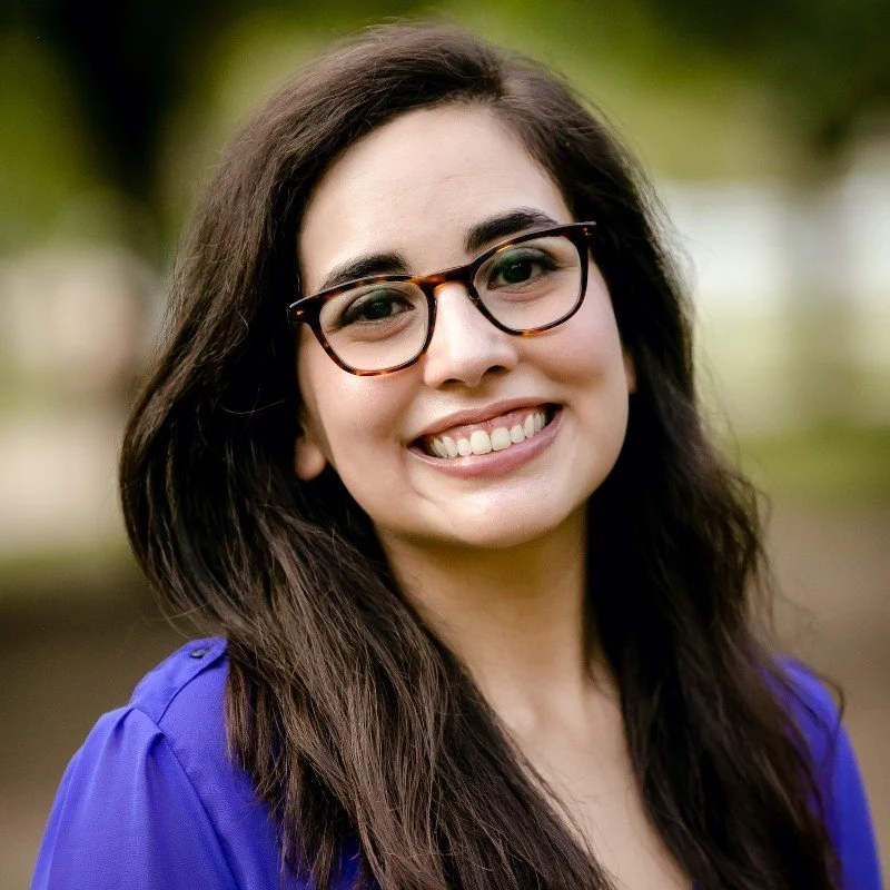 Smiling young woman with glasses and long dark hair outdoors