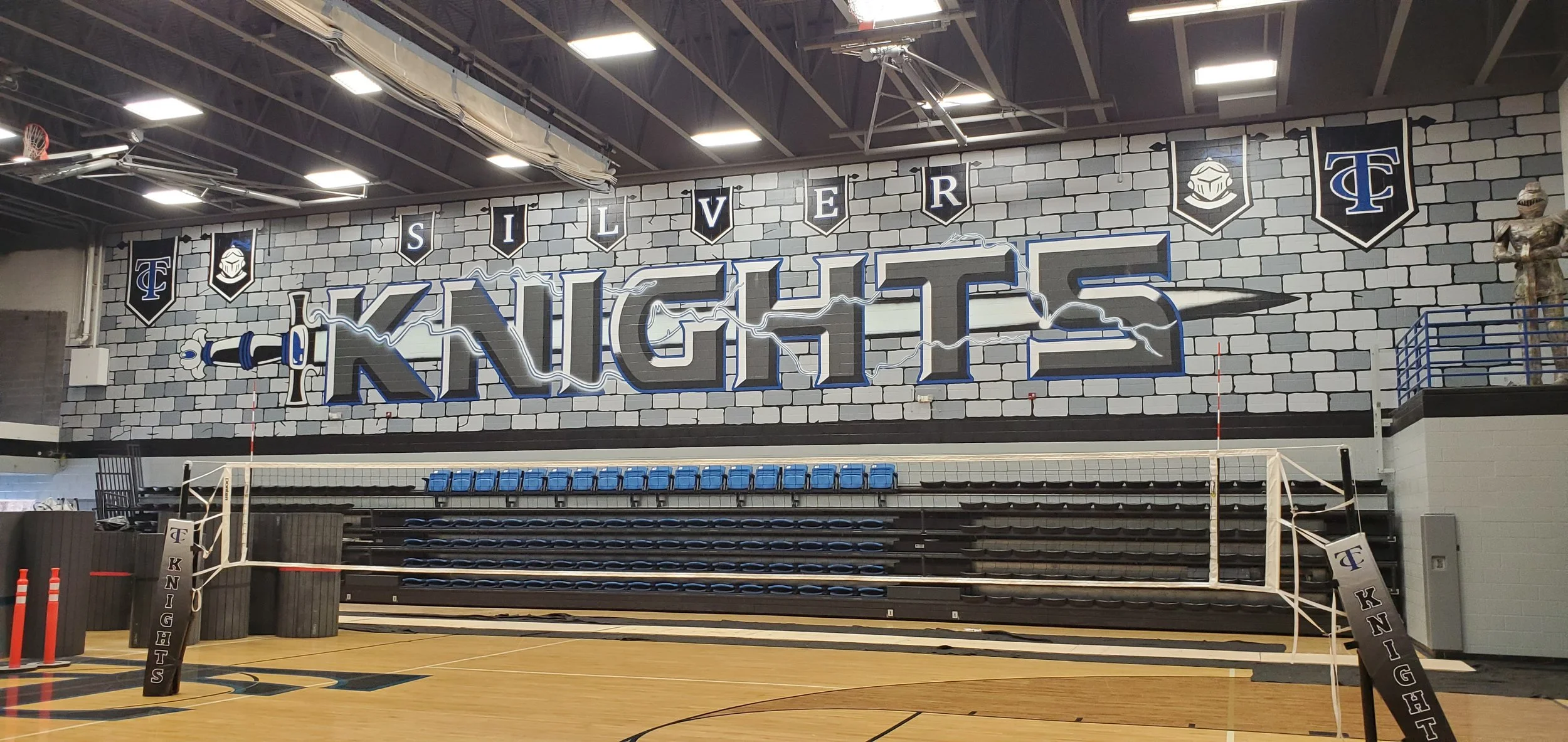 Indoor sports arena with a large wall mural that reads 'Silver Knights' with a knight's sword graphic and shield logos.