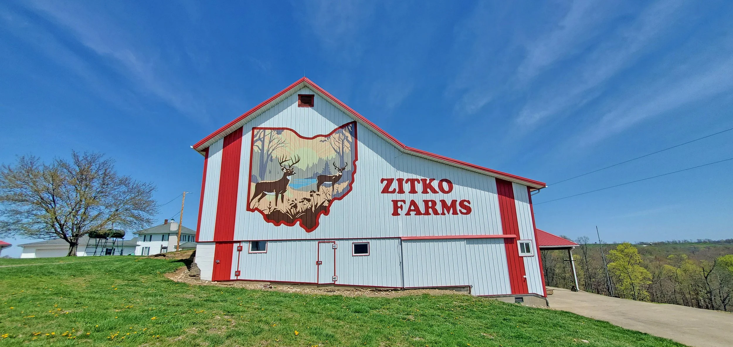 A red and white barn with a mural of a map outline of Ohio, showing two deer in a forest scene, and the words "Zitko Farms".