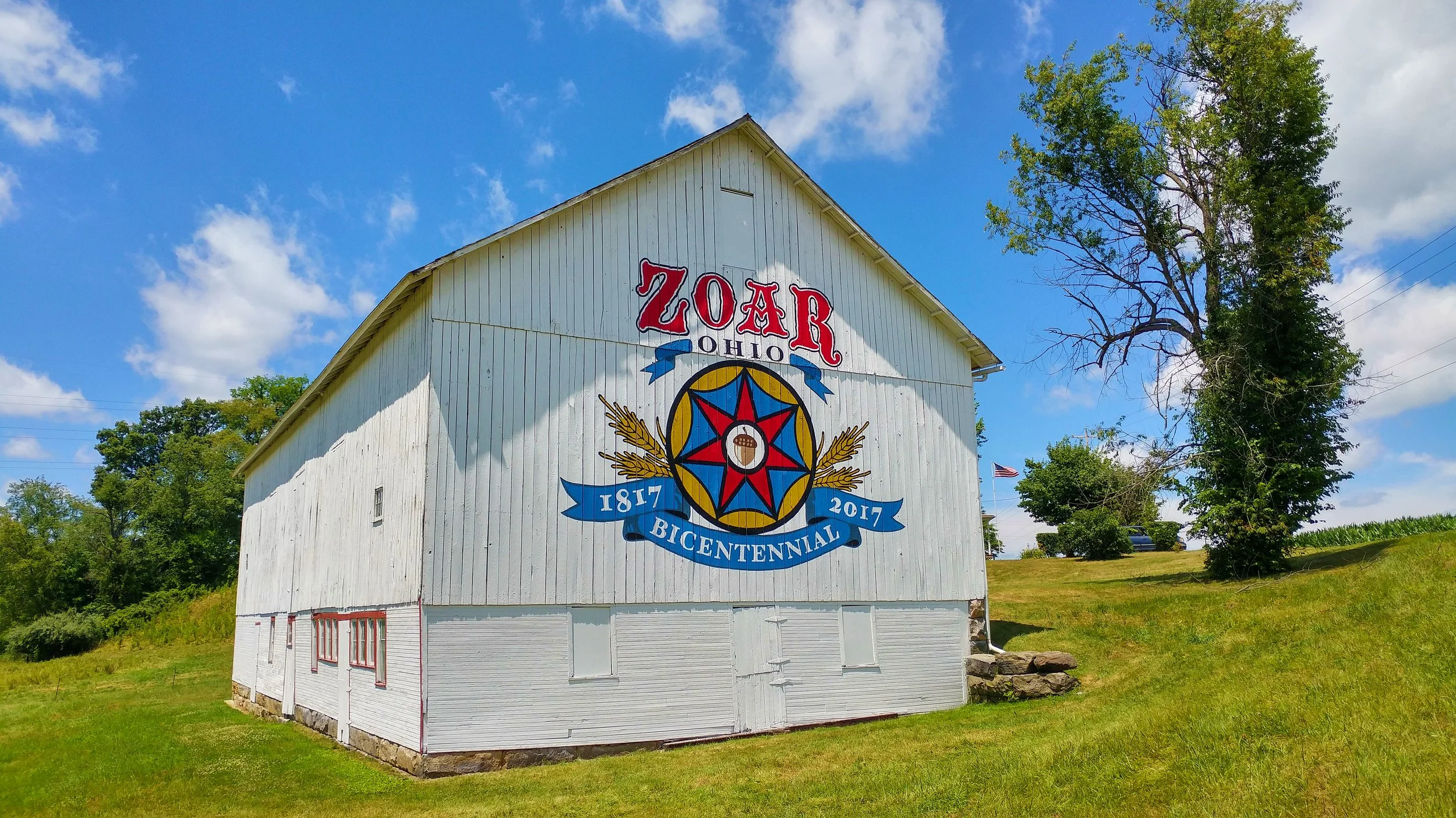 White barn with a painted logo celebrating the Ohio Zoo's bicentennial, with trees and blue sky in the background.
