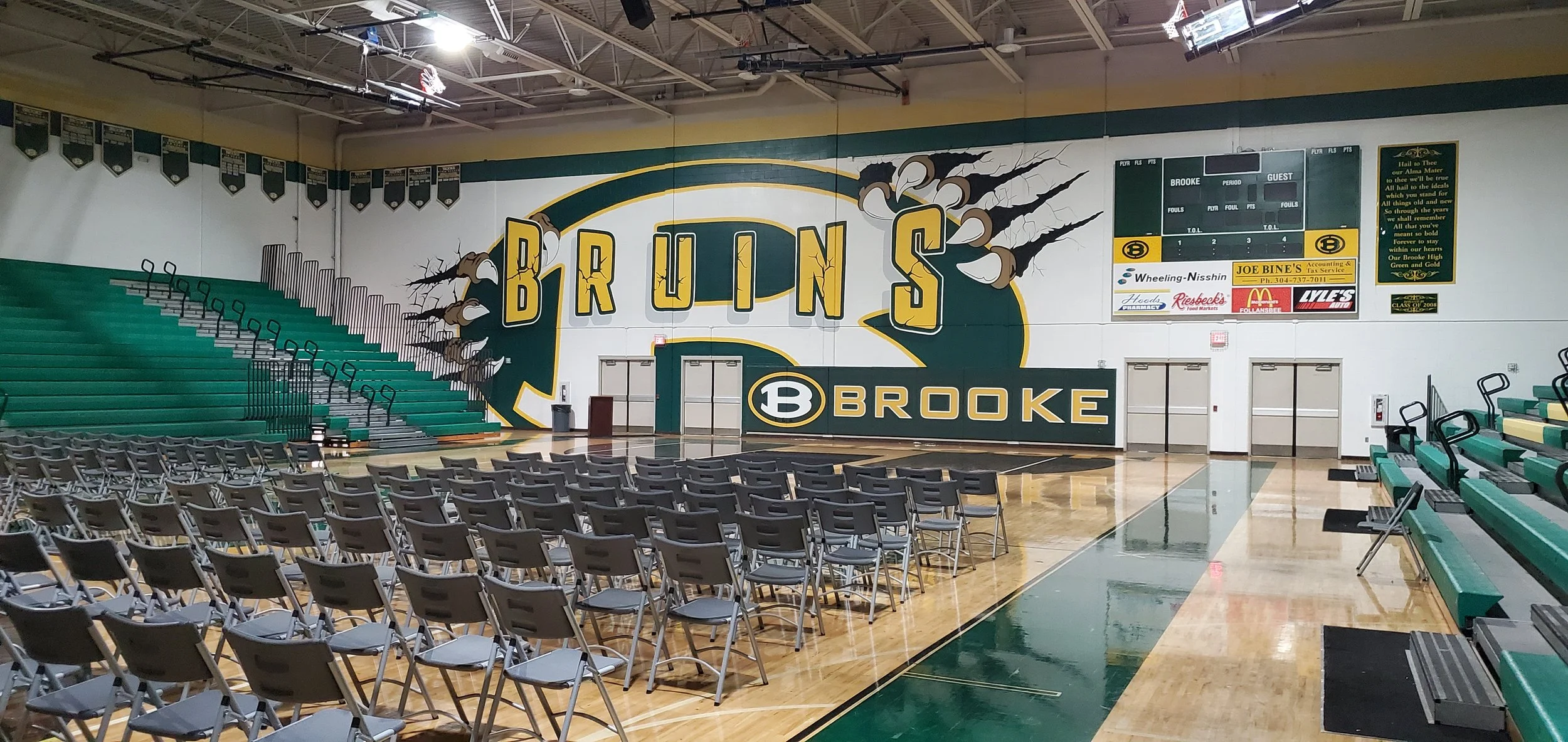 An indoor basketball arena with seating and a large mural on the wall depicting the team name 'Bruins' and mascot claws.