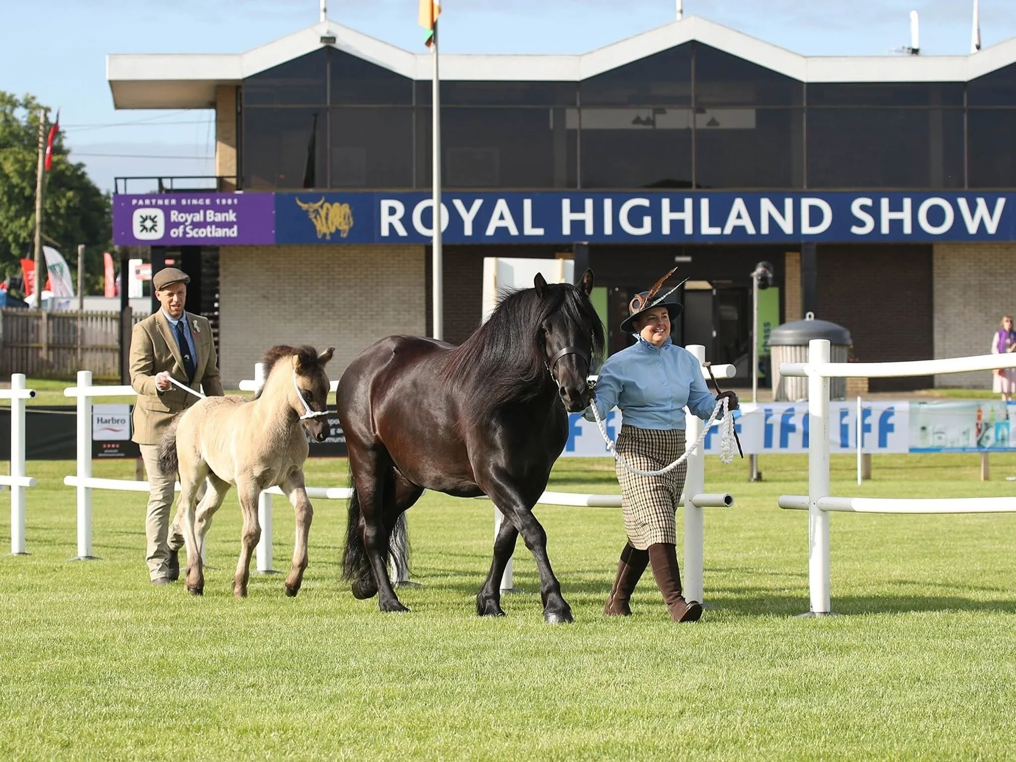 People leading ponies at the Royal Highland Show in Scotland with a large banner in the background.