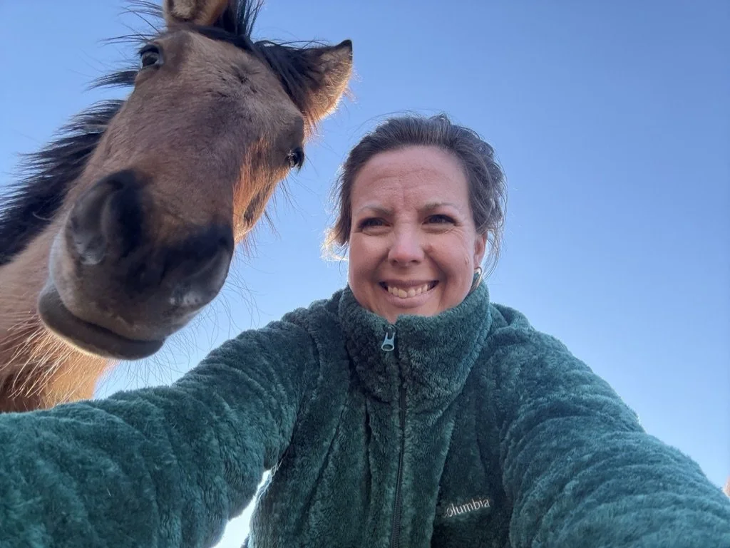 A woman taking a selfie with a horse against a clear blue sky.
