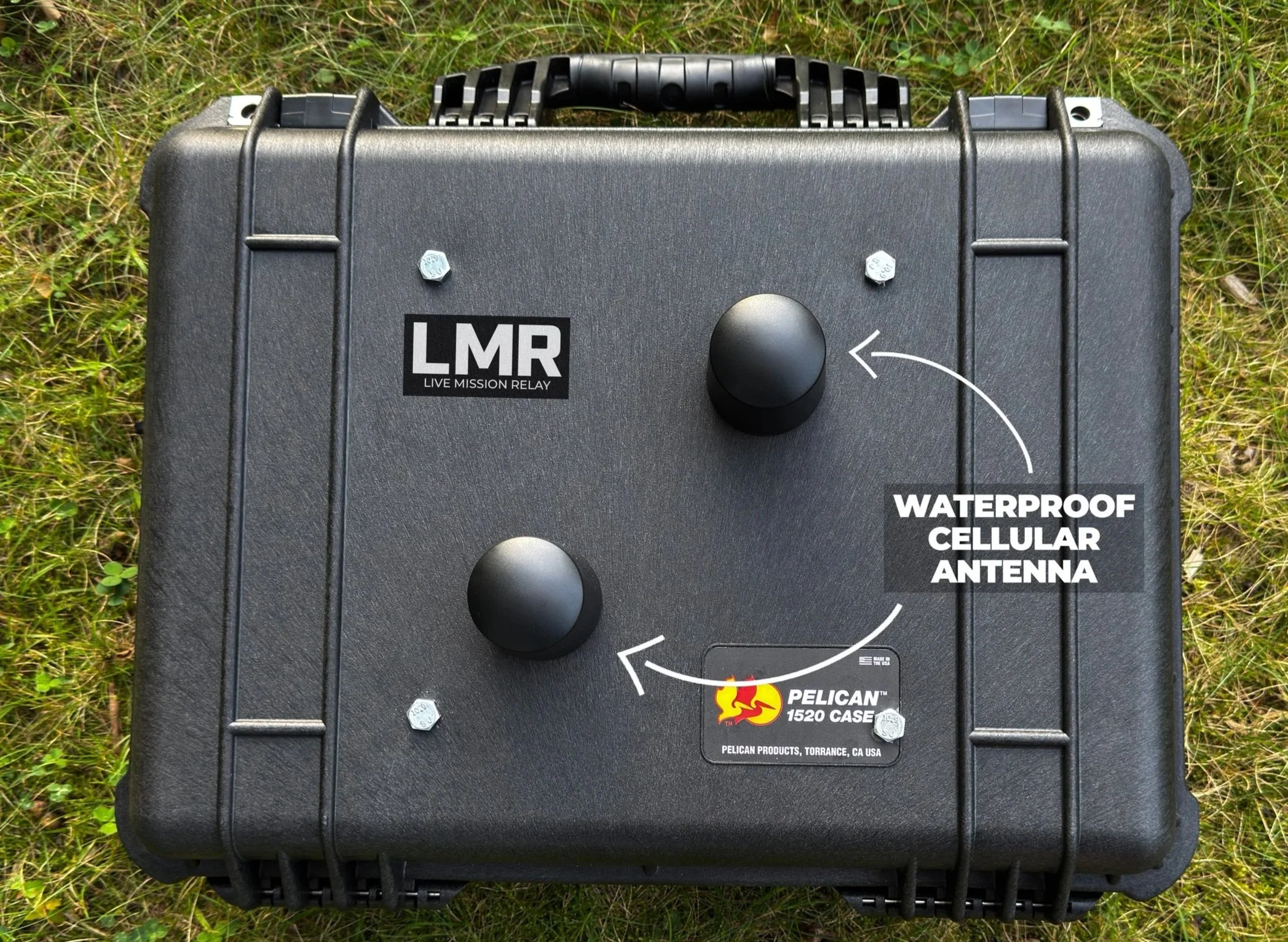 A black waterproof cellular antenna box with a handle on top, labeled with 'LMR Live Mission Relay' and logos for Pelican 1520 case, situated on grass.