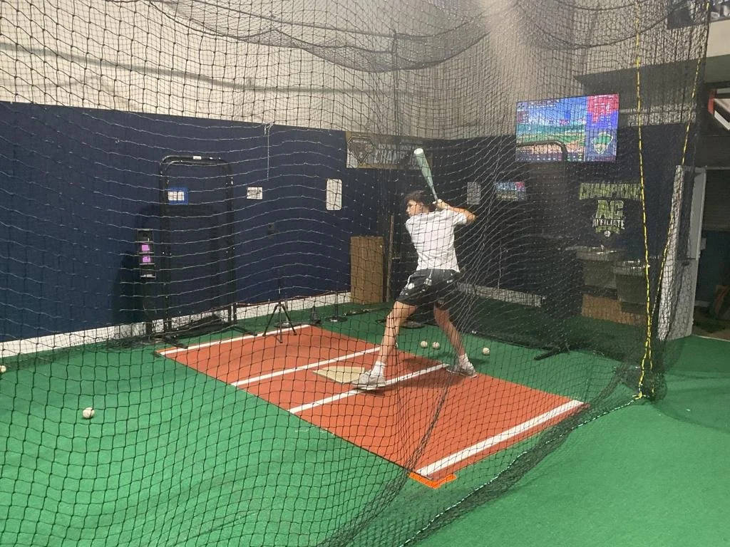 A person practicing baseball batting in an indoor netted training area.