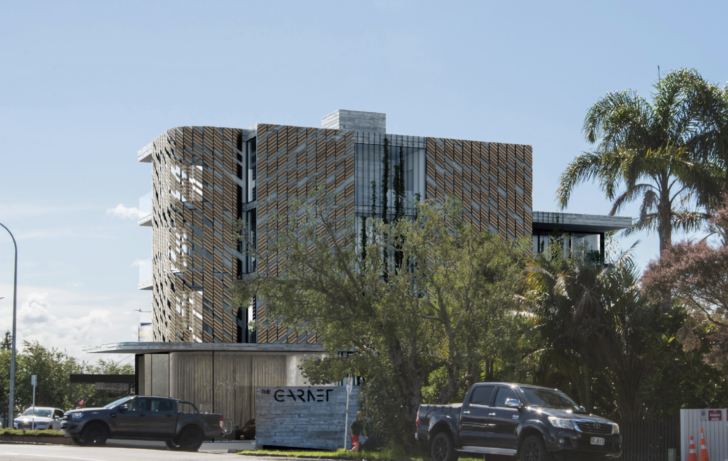 Modern multi-story building with a patterned wooden facade, surrounded by trees and parked vehicles, under a clear blue sky.