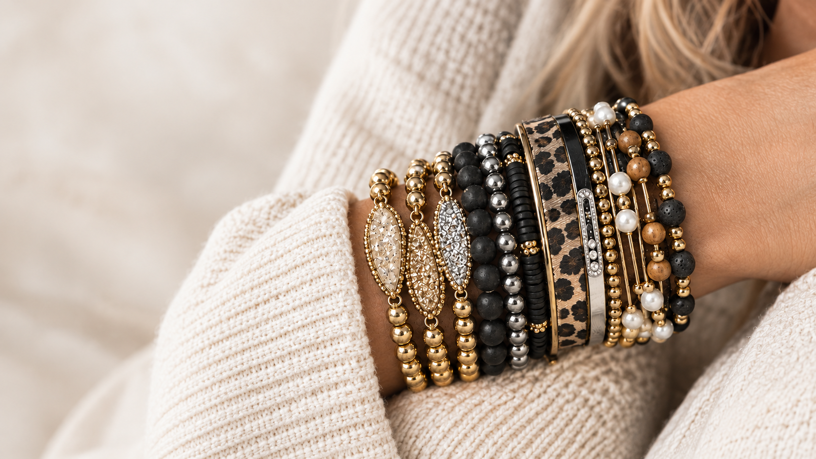 Close-up of a woman's arm wearing multiple yellow, black, white, and animal print bracelets with beads, pearls, and metal accents.