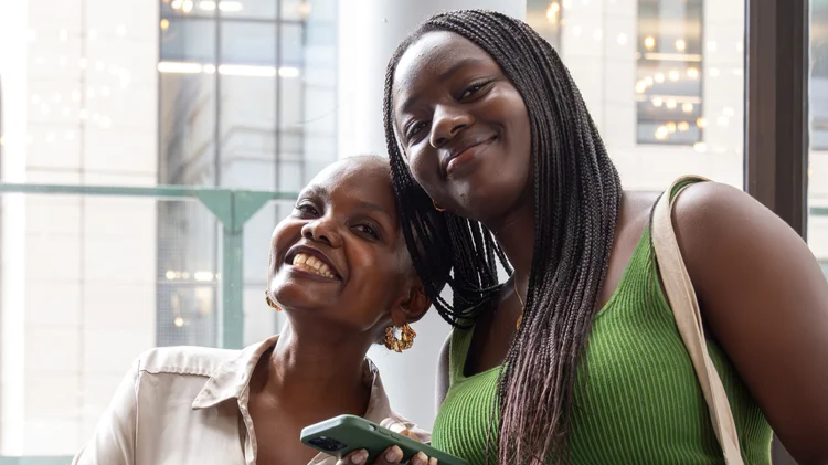 Two women standing side-by-side, smiling at the camera with their heads tilted towards each other.