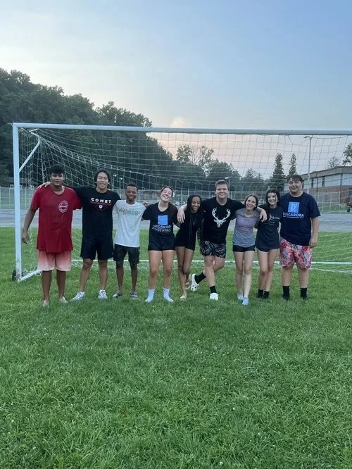 A group of young adults posed in front of a soccer goalpost.