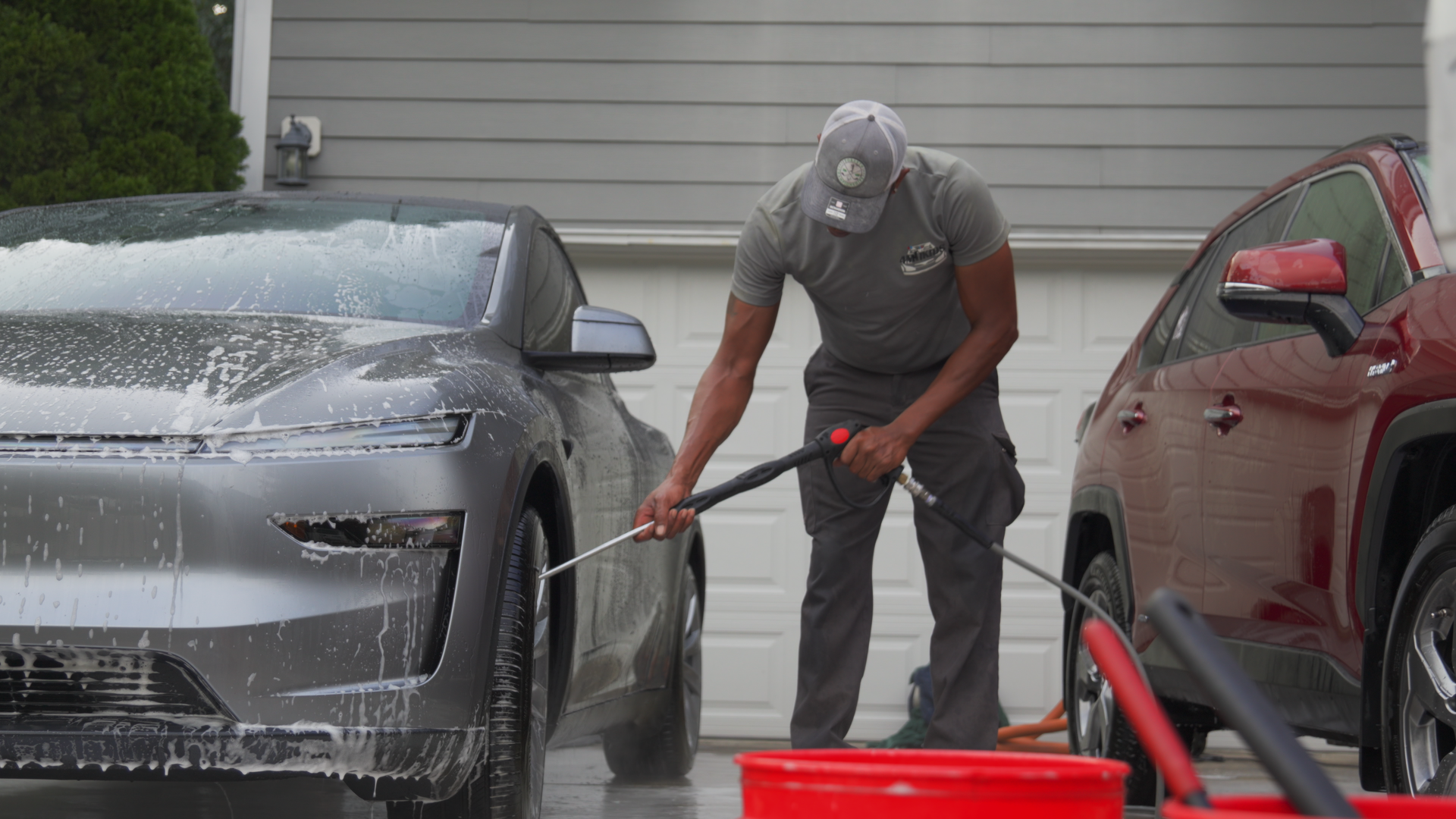 Man cleaning a car with soap in a driveway using a power washer.