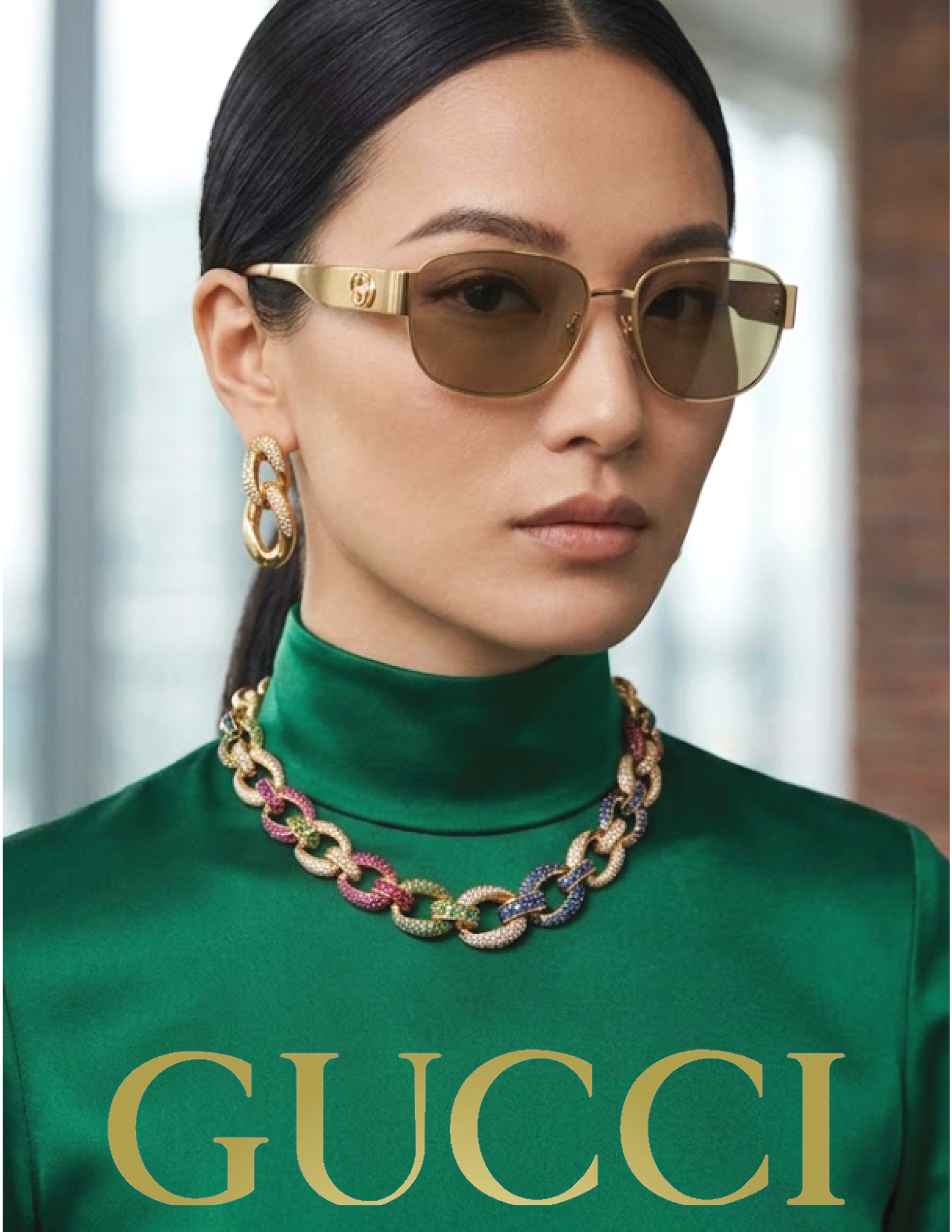 Close-up of a woman with long dark hair, tan sunglasses with gold accents, large gold earrings, a colorful chain necklace, and a green top with gold text reading 'GUCCI'.