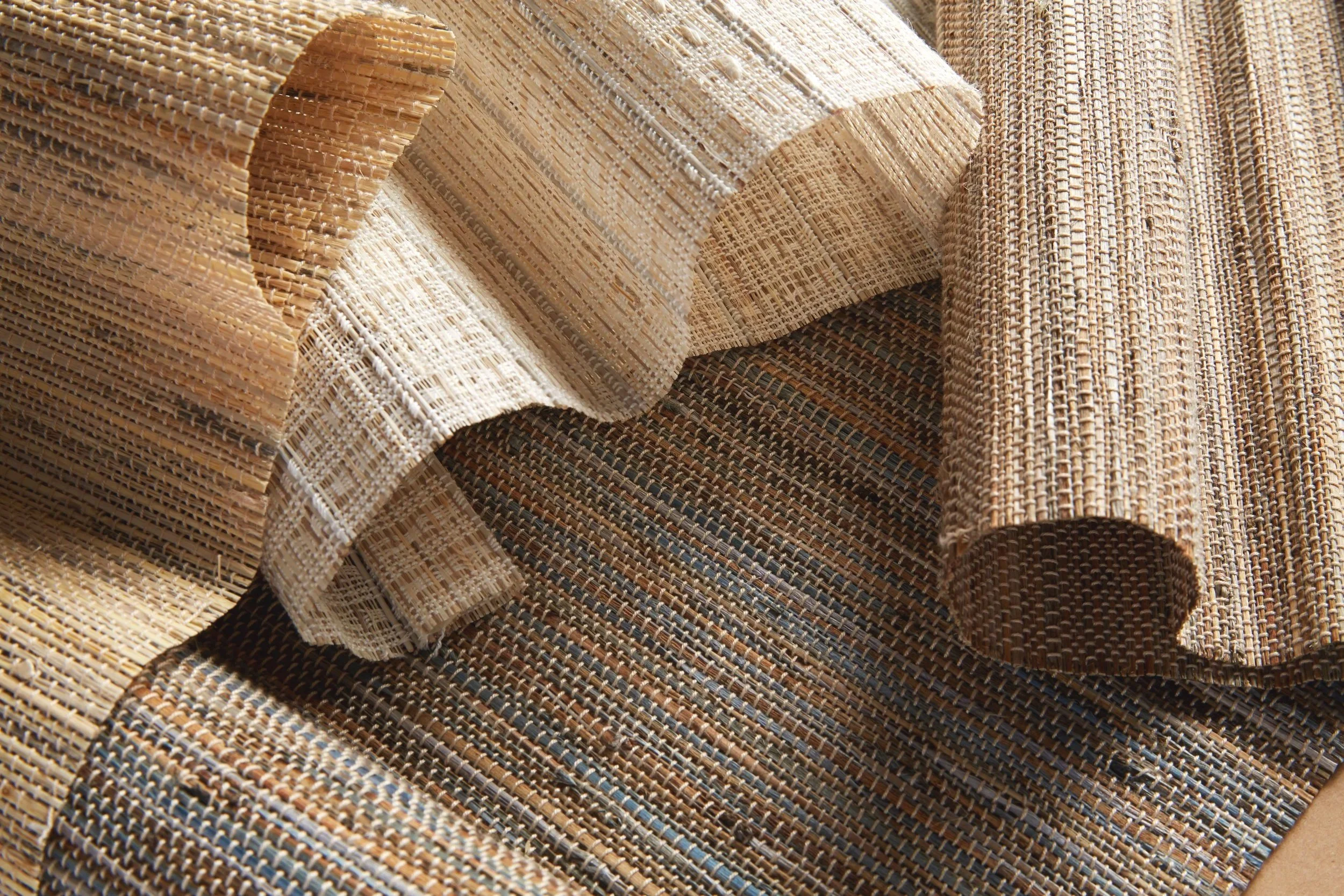 Close-up of rolled, woven straw mats with intricate textured patterns and varying shades of tan, beige, and brown.