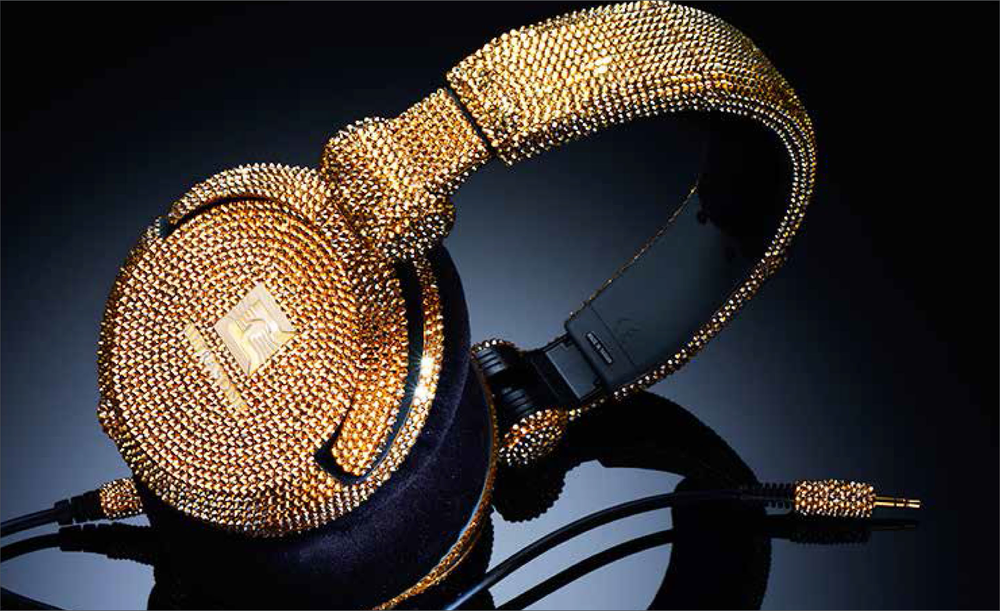 A pair of over-ear headphones decorated with gold and silver rhinestones or crystals, resting on a reflective surface.