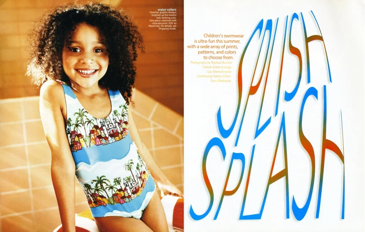 A young girl with curly hair smiling, wearing a colorful swimsuit with a pattern of beaches, palm trees, and houses, sitting in front of a tiled wall, next to a sign that says "Kids Beach Splash" in large, colorful, stylized letters.